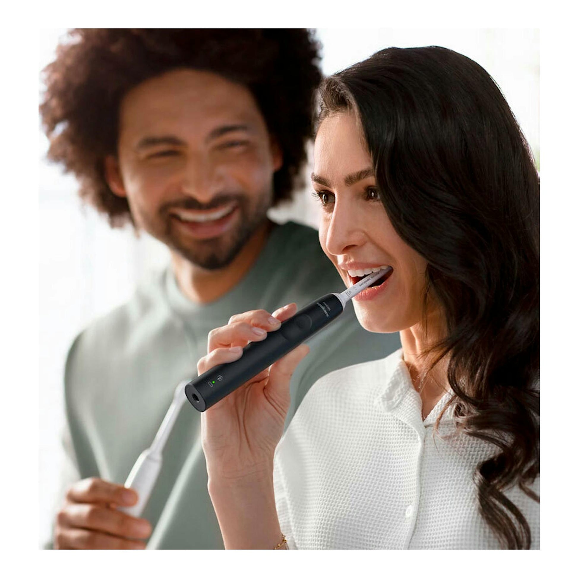 Cepillo dental eléctrico Philips HX3671/14 negro, en uso por una mujer; un hombre sonríe al fondo.
