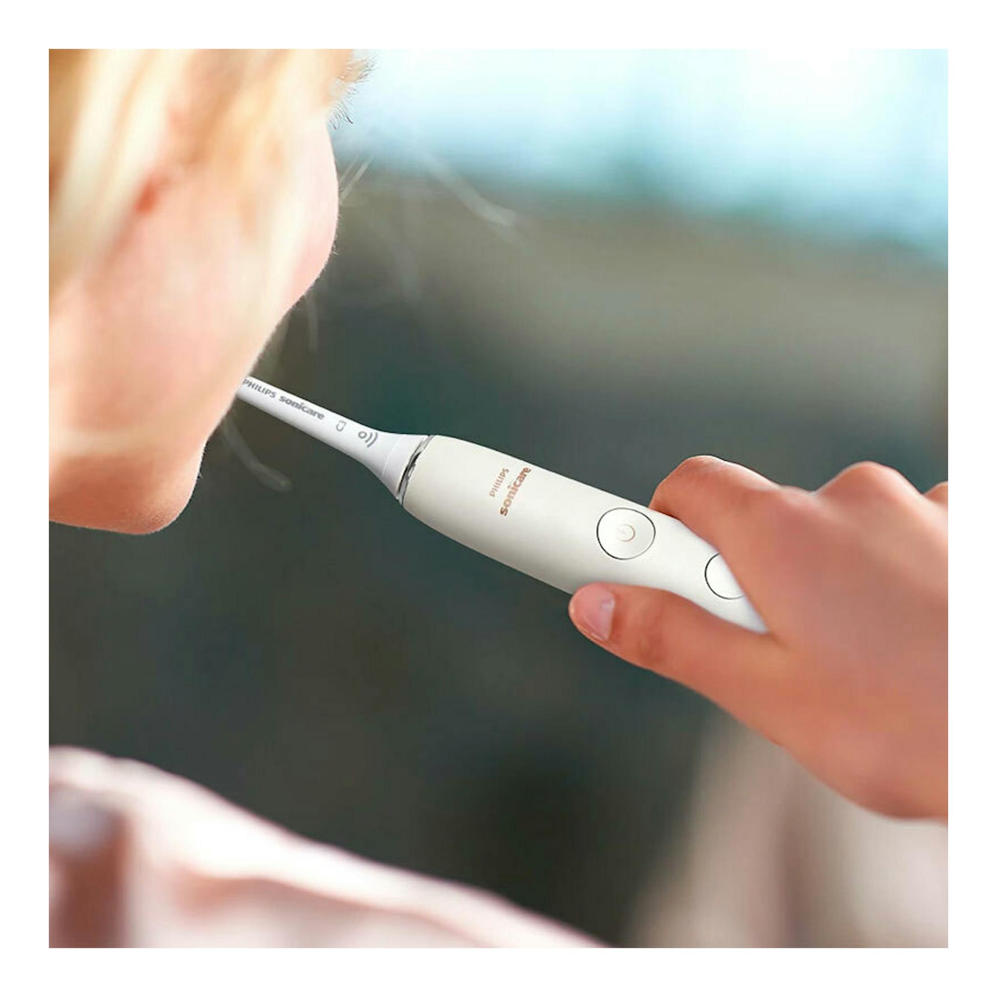 Cepillo dental eléctrico Philips Sonicare blanco, en primer plano, junto a la boca de una persona.