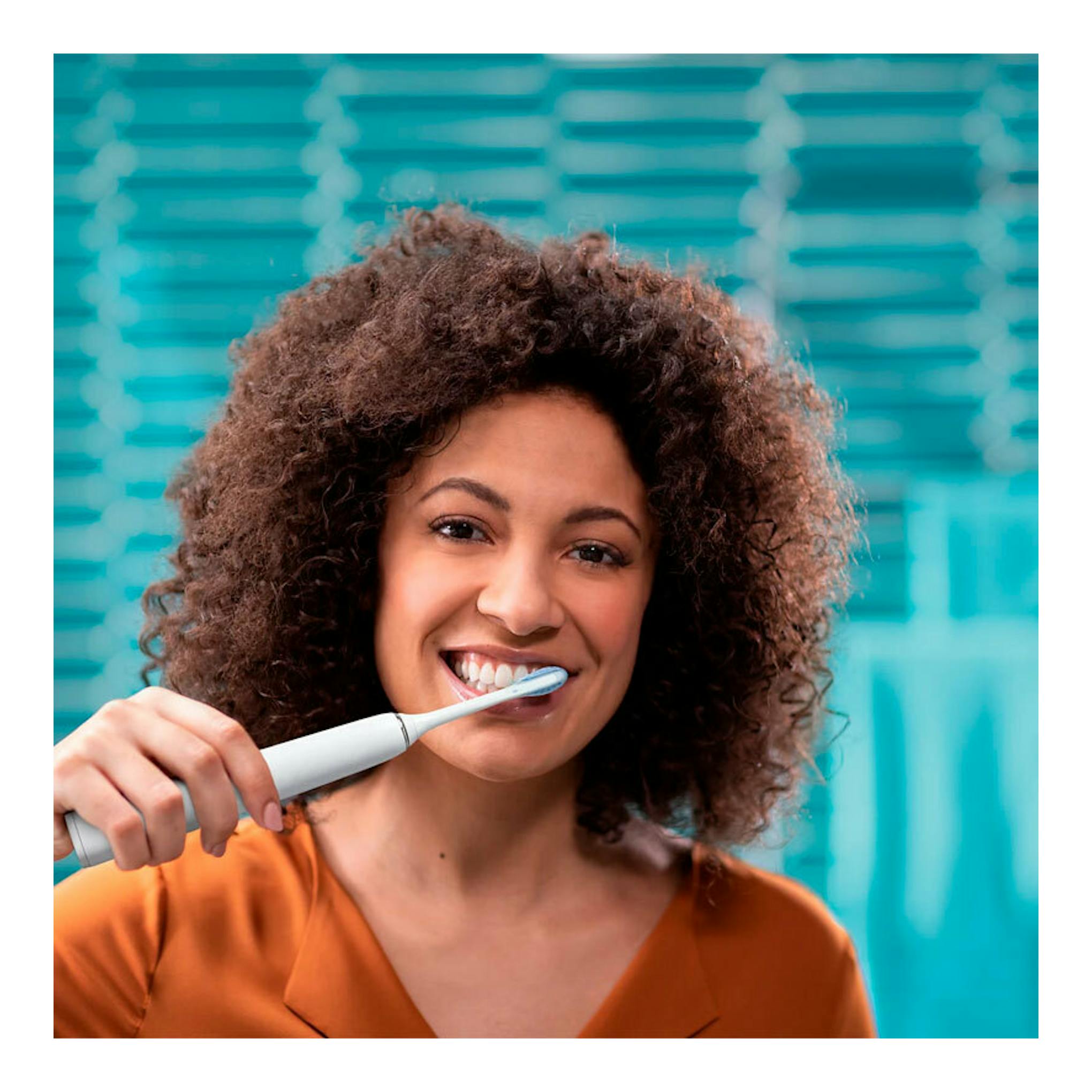 Mujer sonriendo cepillándose los dientes con cepillo dental eléctrico Philips HX9913/17, vista frontal.