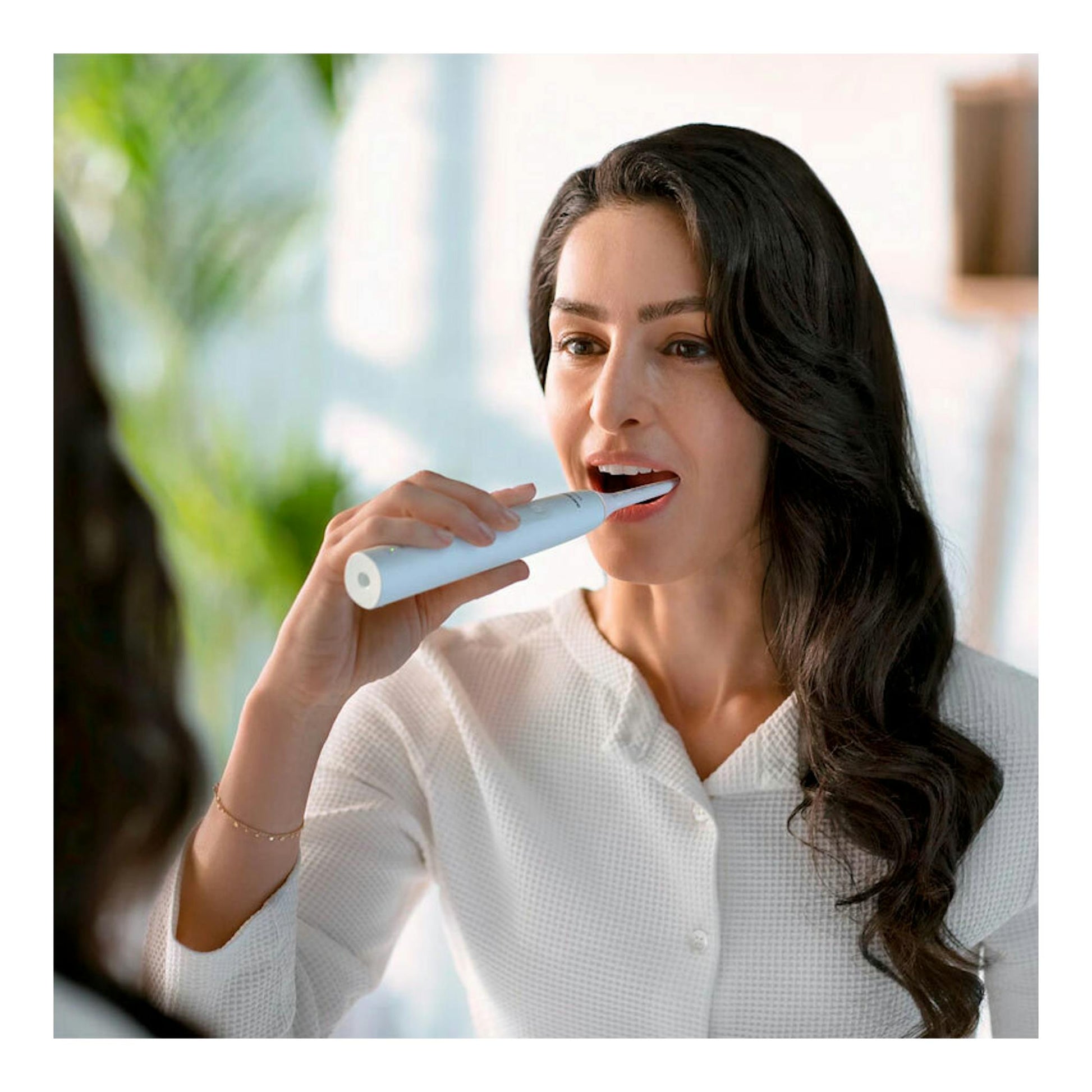 Mujer cepillándose con cepillo dental eléctrico blanco Philips HX3681/33, vista frontal.