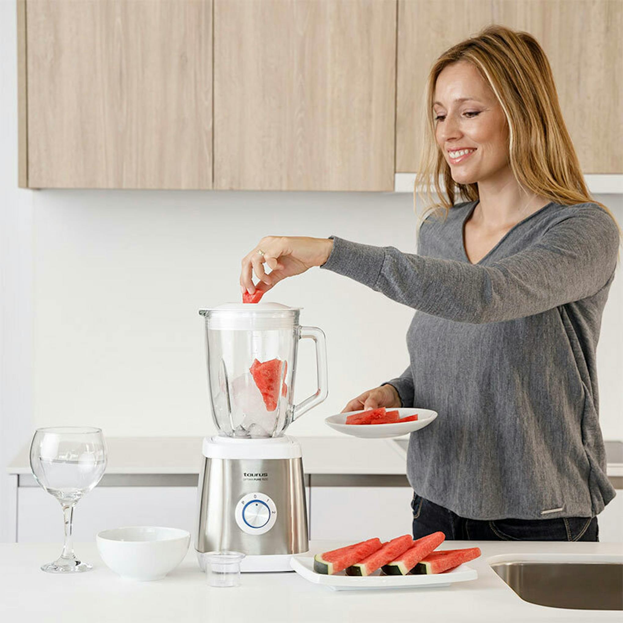 Batidora de vaso Taurus Optima Pure 1500 en una cocina, con una mujer colocando fruta
