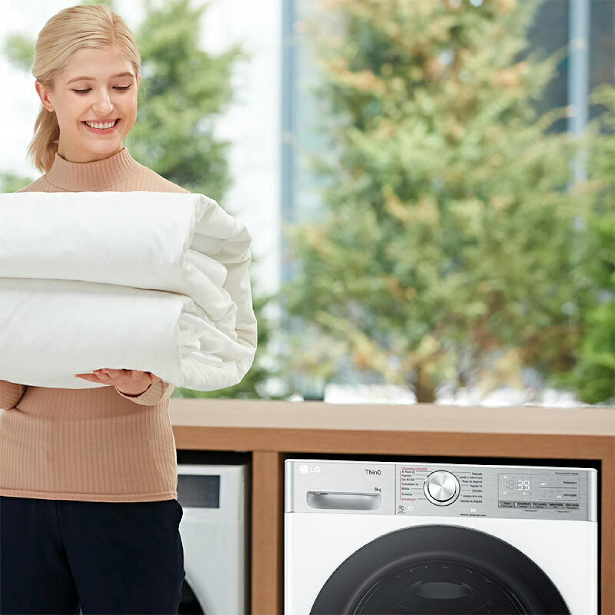 Lavadora LG F4WR9009A2W de carga frontal junto a una mujer con ropa doblada