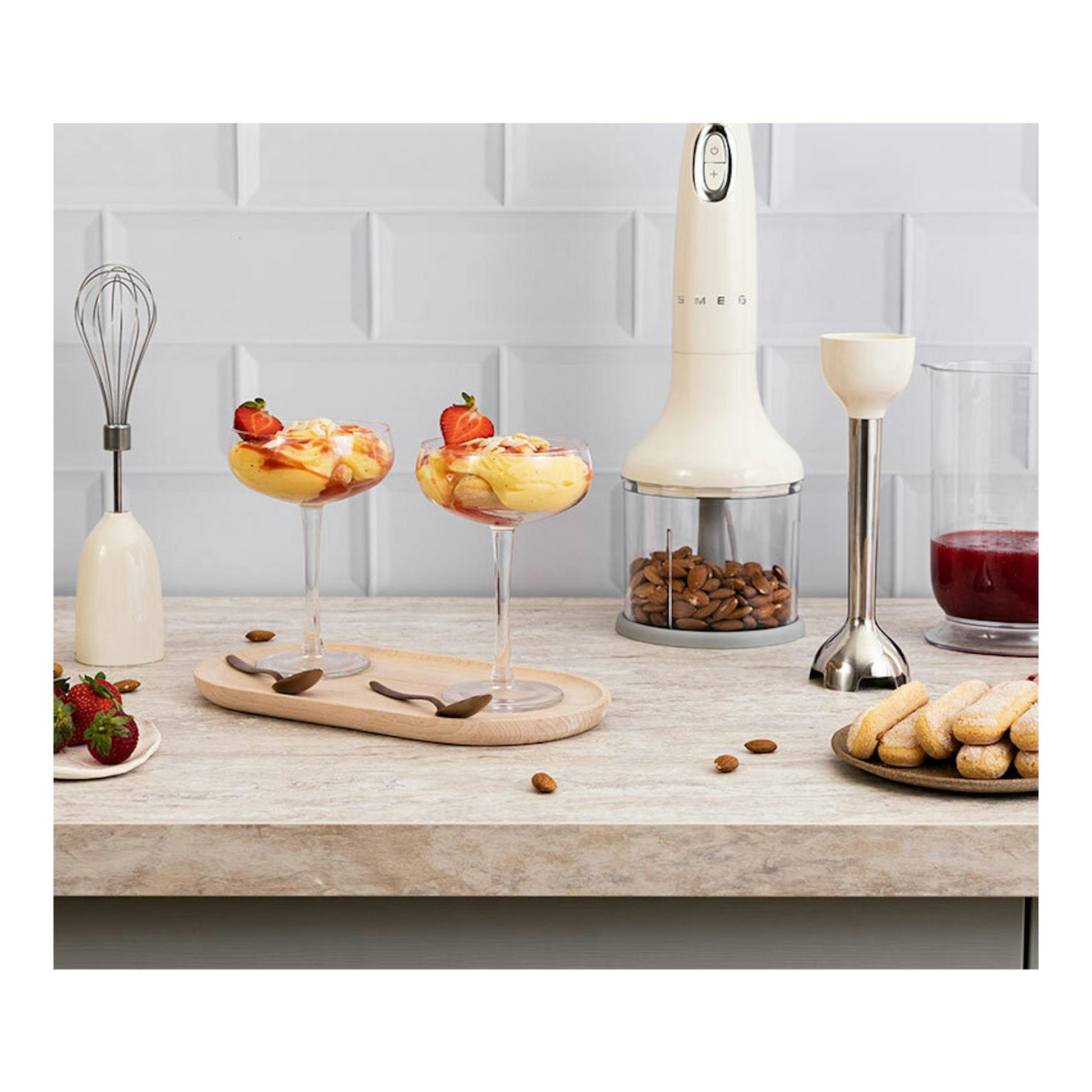Batidora de mano Smeg HBF03CREU crema, vista frontal, con accesorios sobre una encimera de cocina.