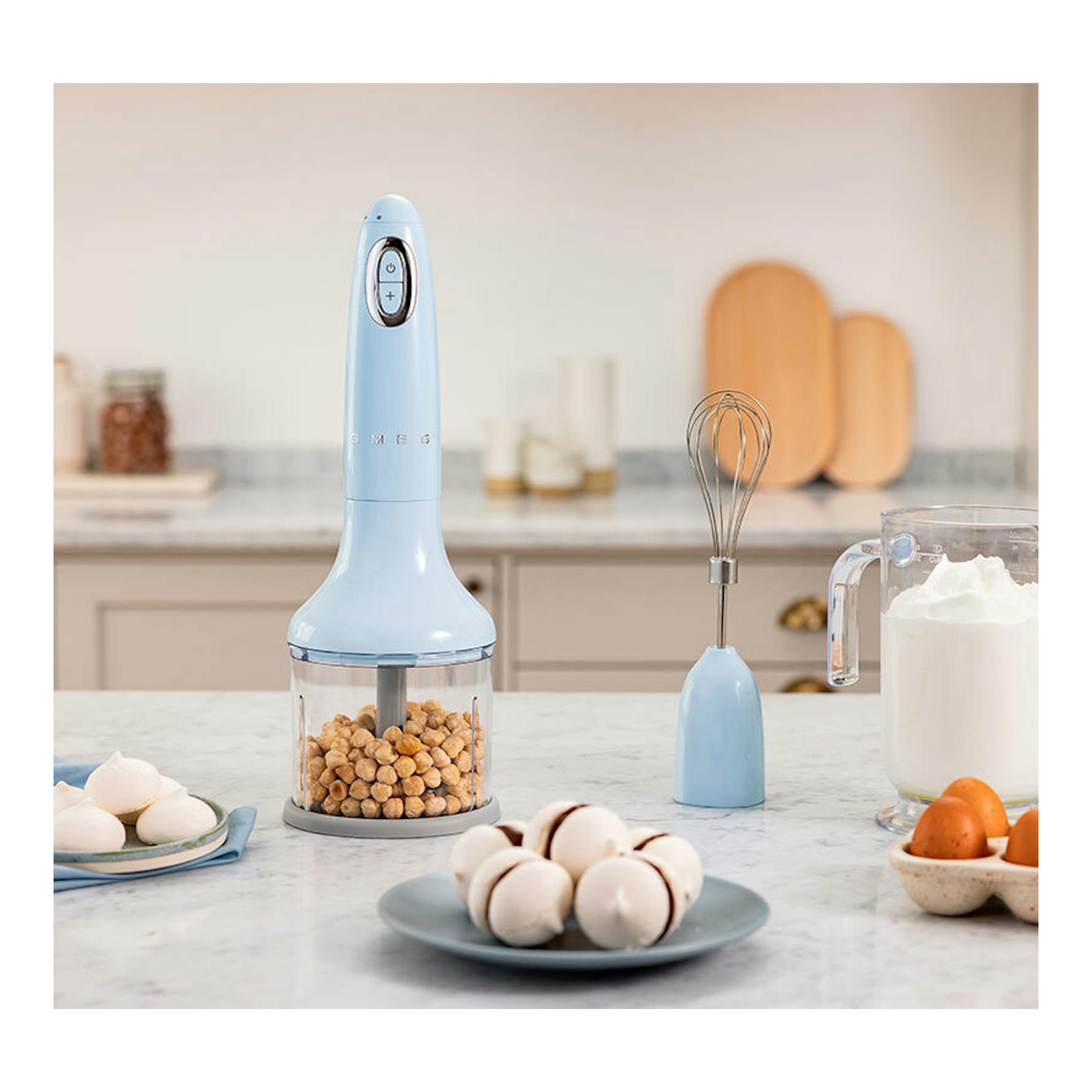 Batidora de mano Smeg HBF03PBEU azul pastel, vista frontal con vaso picador y varilla sobre encimera.