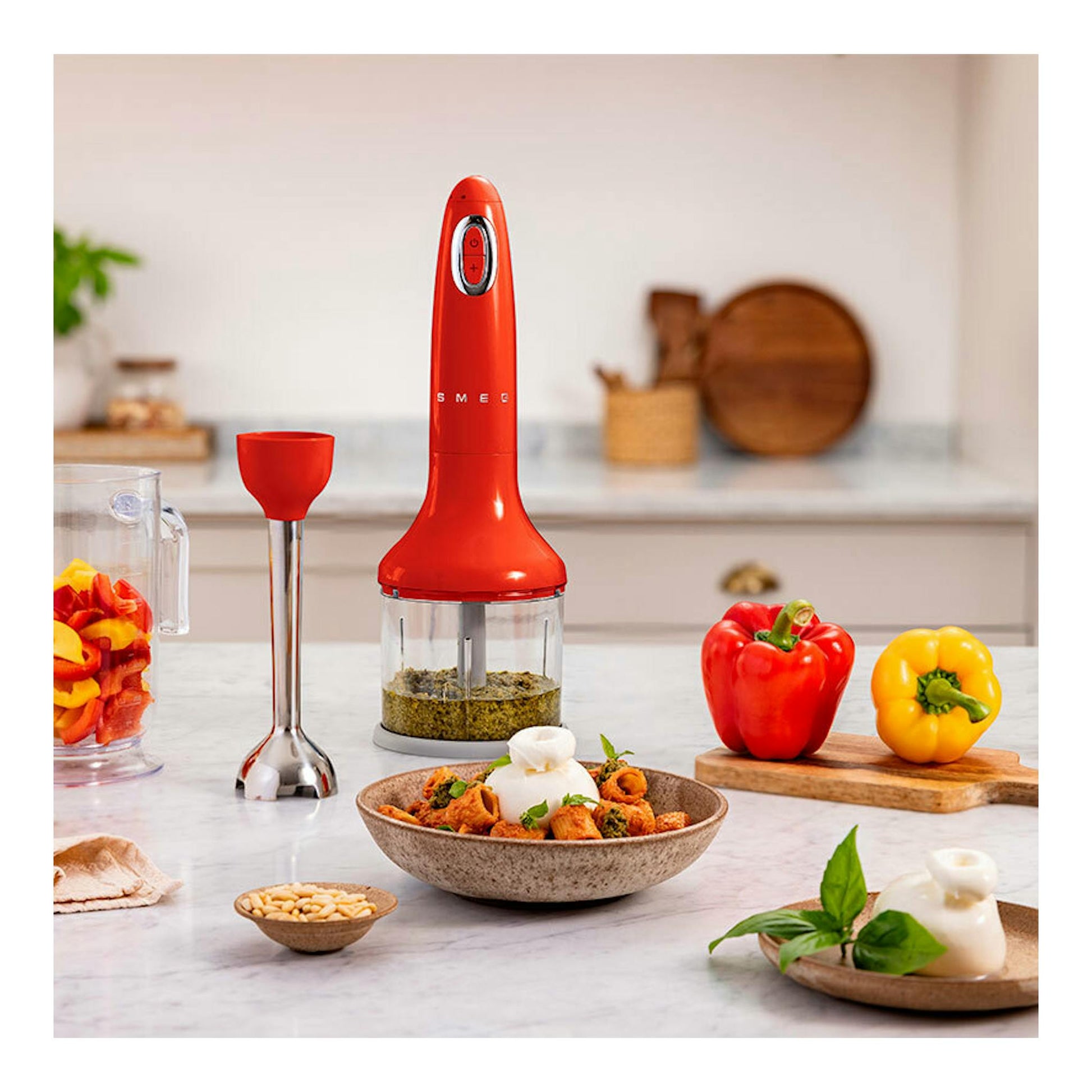 Batidora de mano Smeg HBF03RDEU roja, vista frontal, con vaso medidor y accesorios sobre encimera.