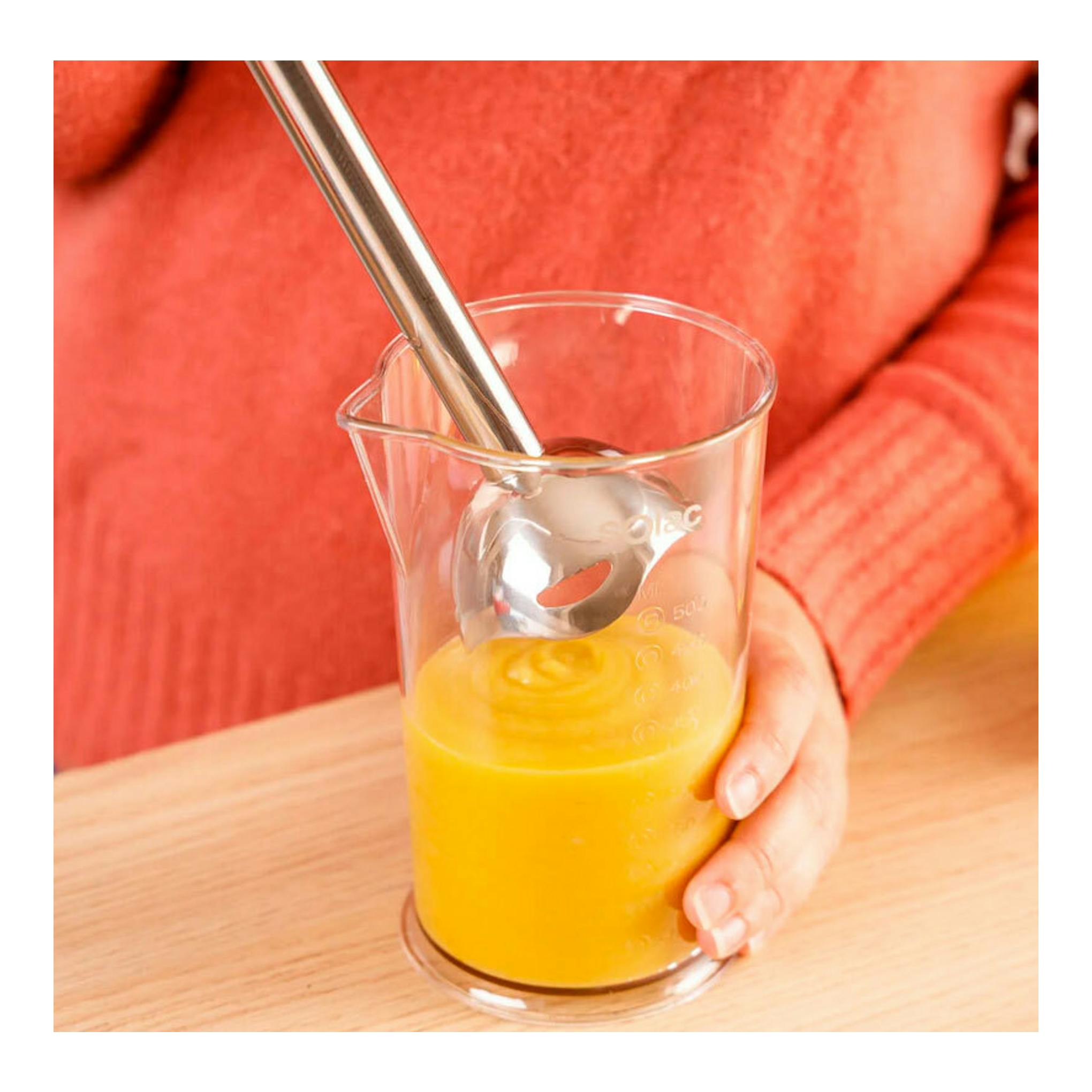 Batidora de mano Solac BA5614 en un vaso medidor, mezclando puré naranja, vista frontal.