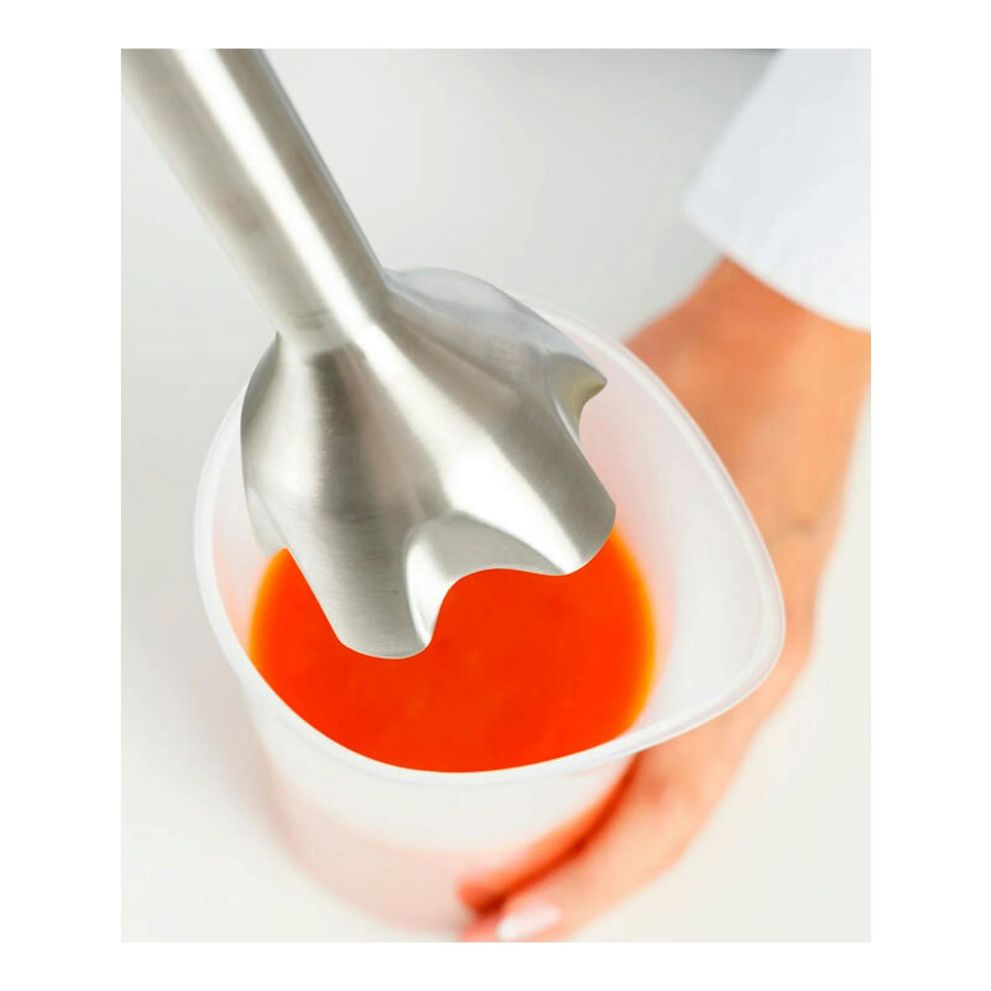 Batidora de mano Taurus Bapi 1500 Inox, vista cenital, batiendo líquido naranja en vaso medidor transparente.