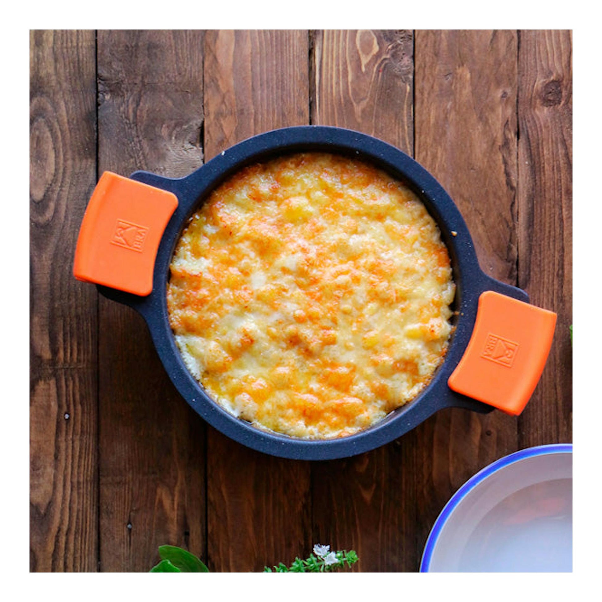 Cacerola baja Bra Efficient negra con asas naranjas, vista cenital, con gratinado dorado sobre mesa de madera.