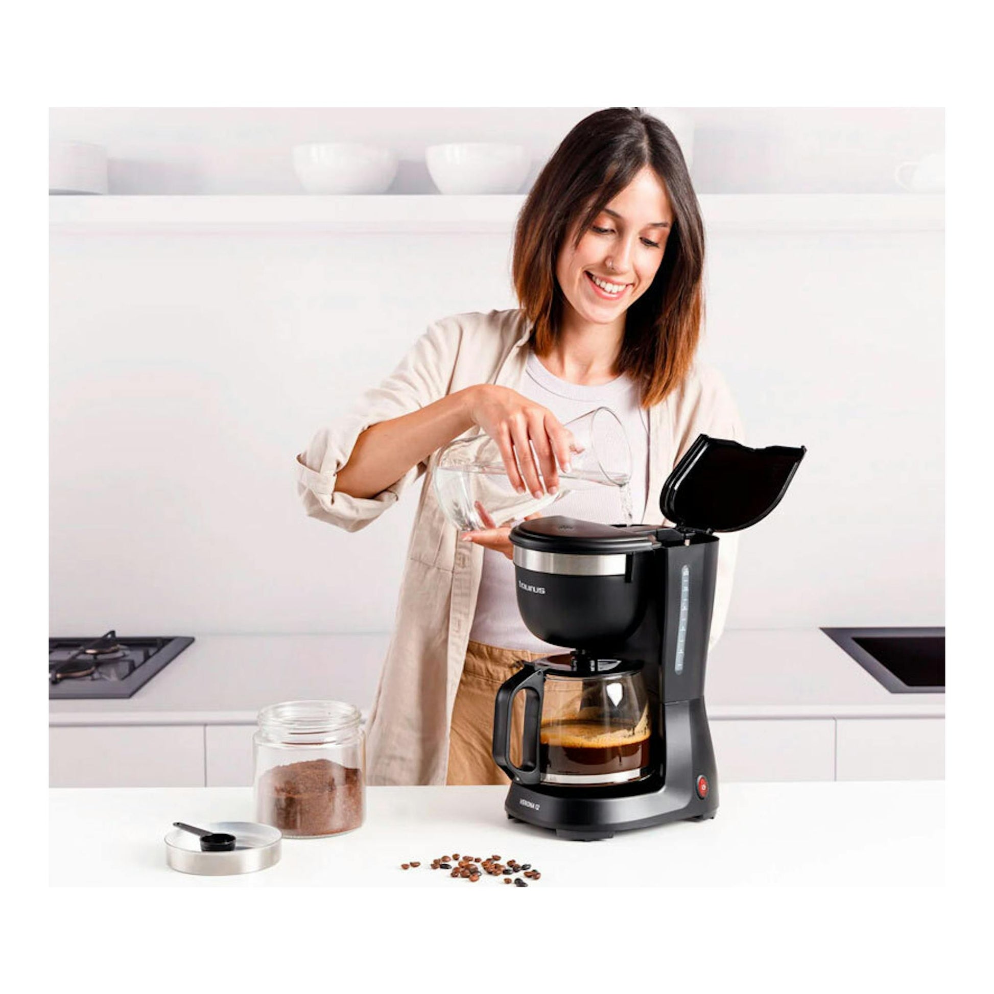 Cafetera de goteo Taurus Verona 12 negra, vista frontal, con jarra de vidrio y una mujer vertiendo agua.