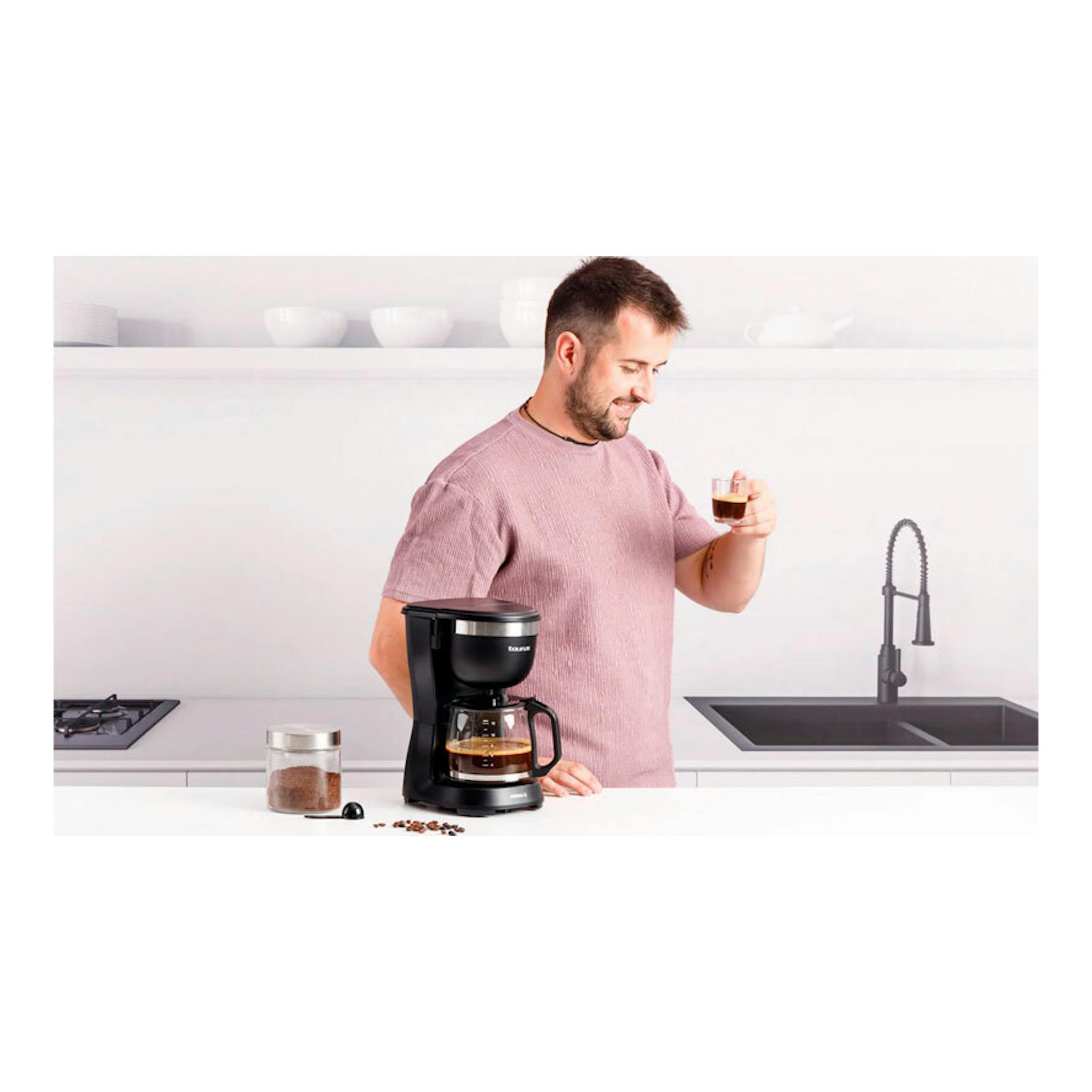 Cafetera de goteo Taurus Verona 12 negra, vista frontal, sobre una encimera de cocina junto a un hombre con una taza.