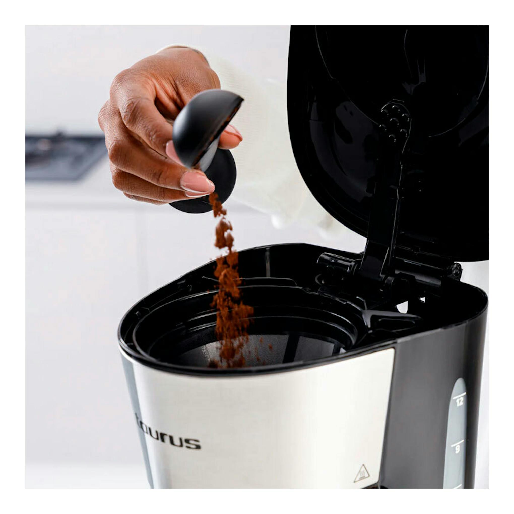 Cafetera de goteo Taurus Verona 12 Inox, negra y acero, con tapa abierta y café molido cayendo al filtro.