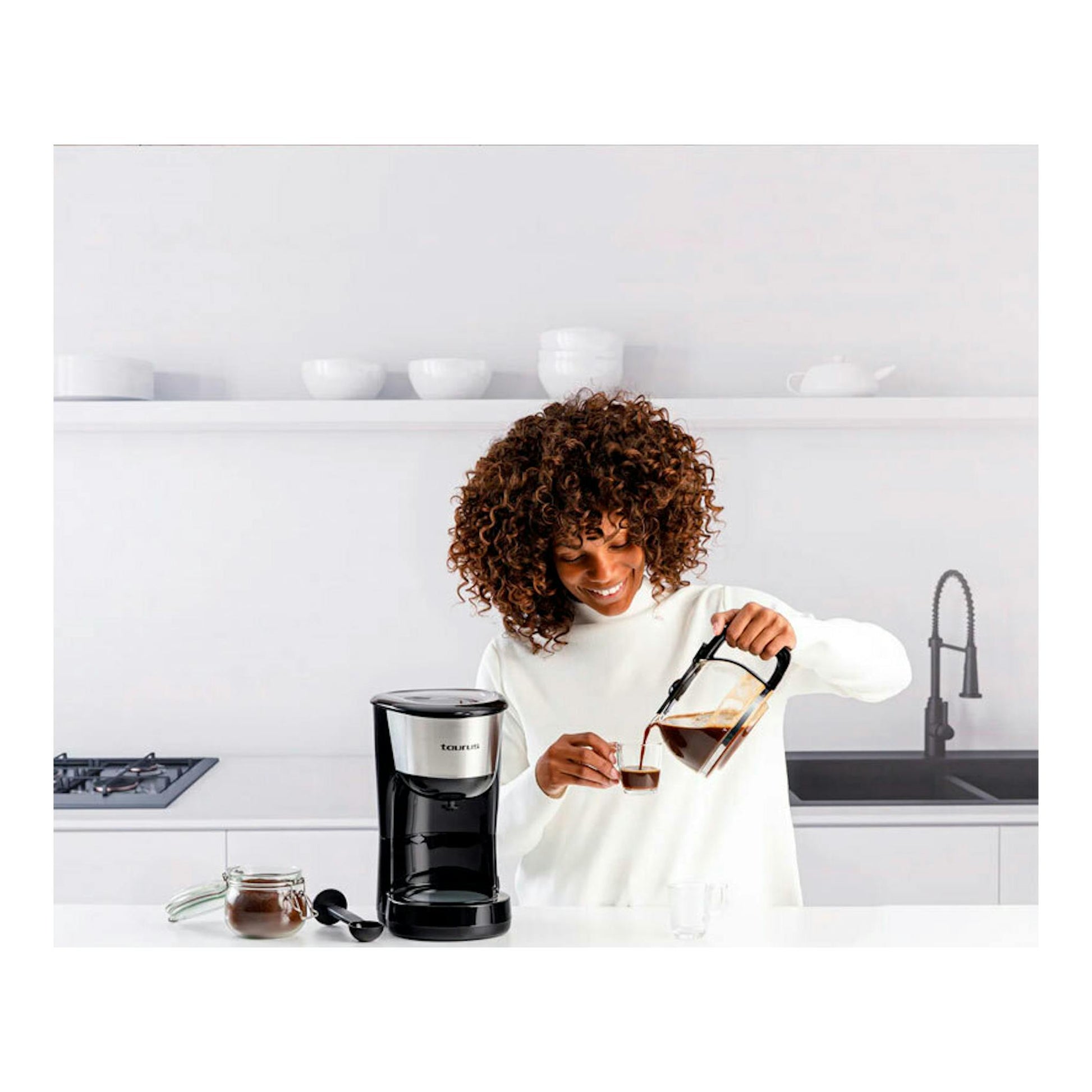 Cafetera de goteo Taurus Verona 12 Inox negra y acero, con una mujer sirviendo café en una cocina blanca.