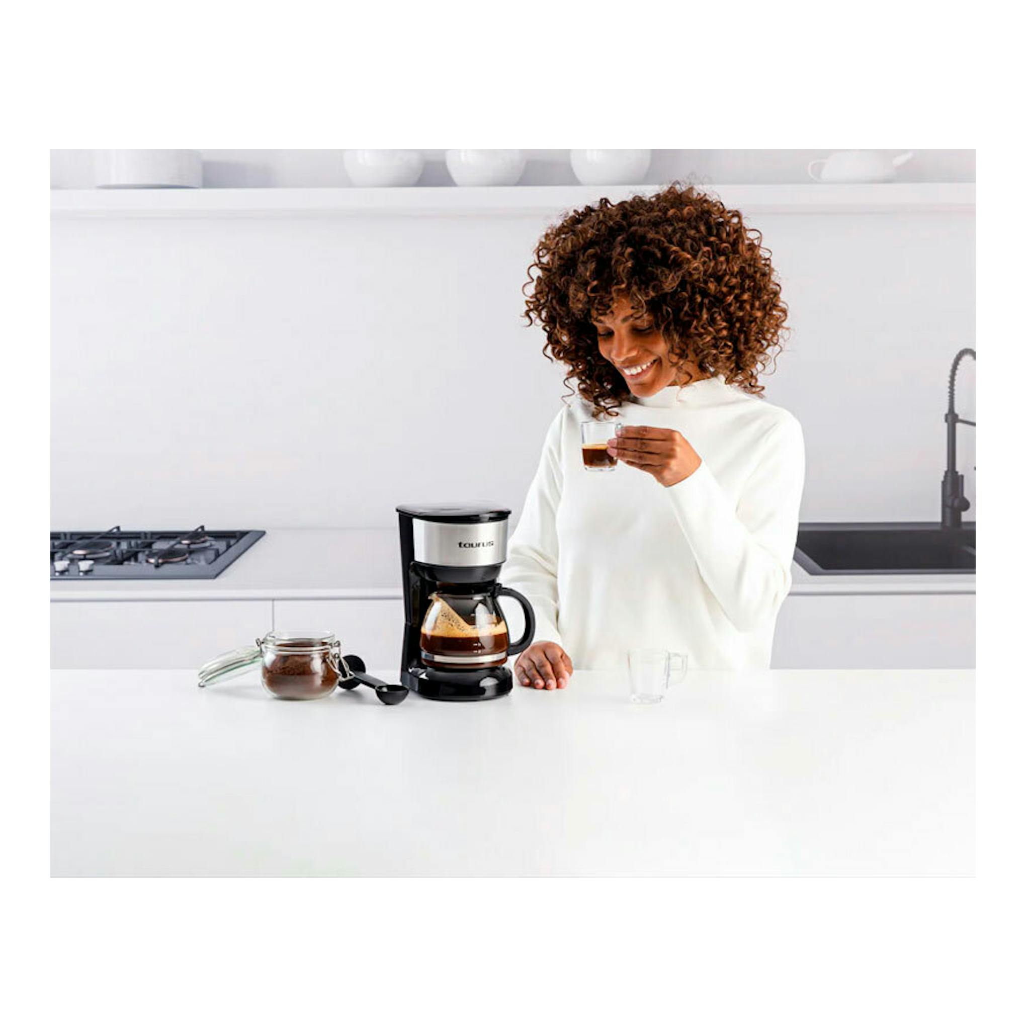 Cafetera de goteo Taurus Verona 6 Inox negra y acero, vista frontal, con jarra y una mujer sirviéndose.