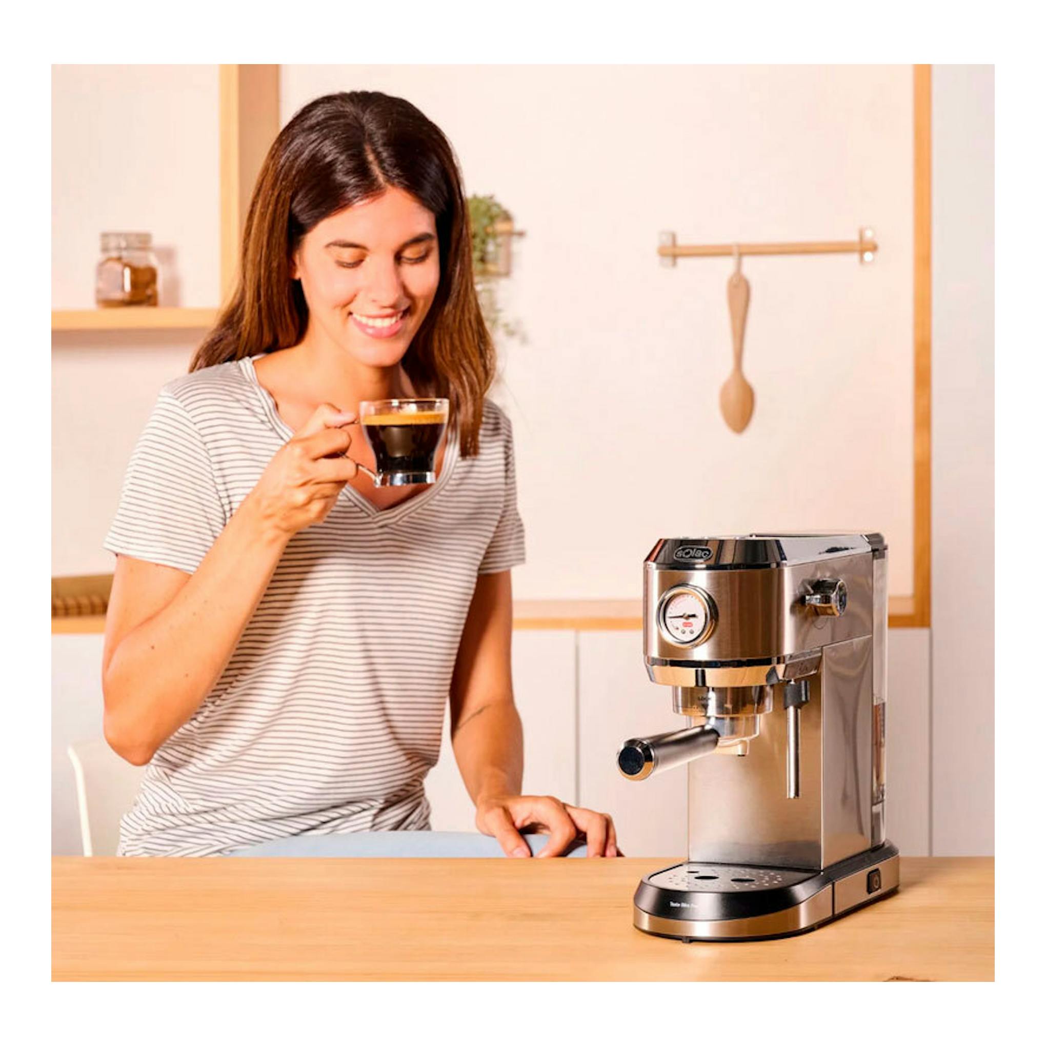 Cafetera espresso Solac CE4520 de acero inoxidable, vista frontal, sobre una mesa junto a una mujer con una taza.