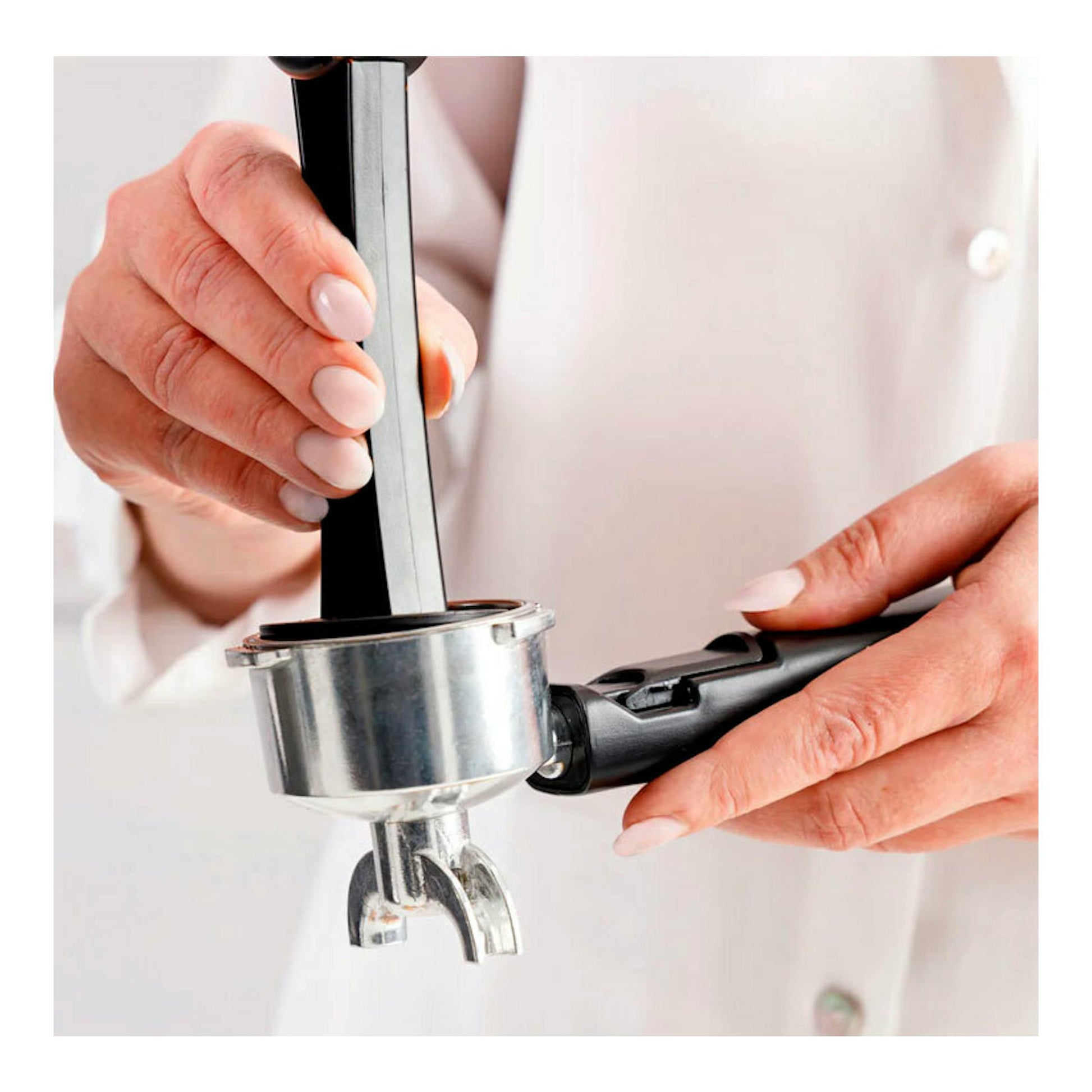 Primer plano de unas manos sujetando el portafiltro metálico y negro de una cafetera espresso.