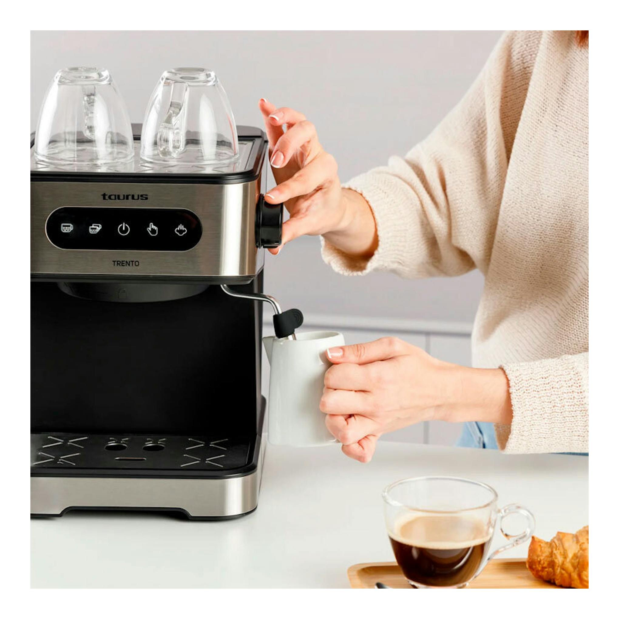 Cafetera espresso Taurus Trento negra y acero, vista frontal, con una persona colocando una taza bajo el surtidor.