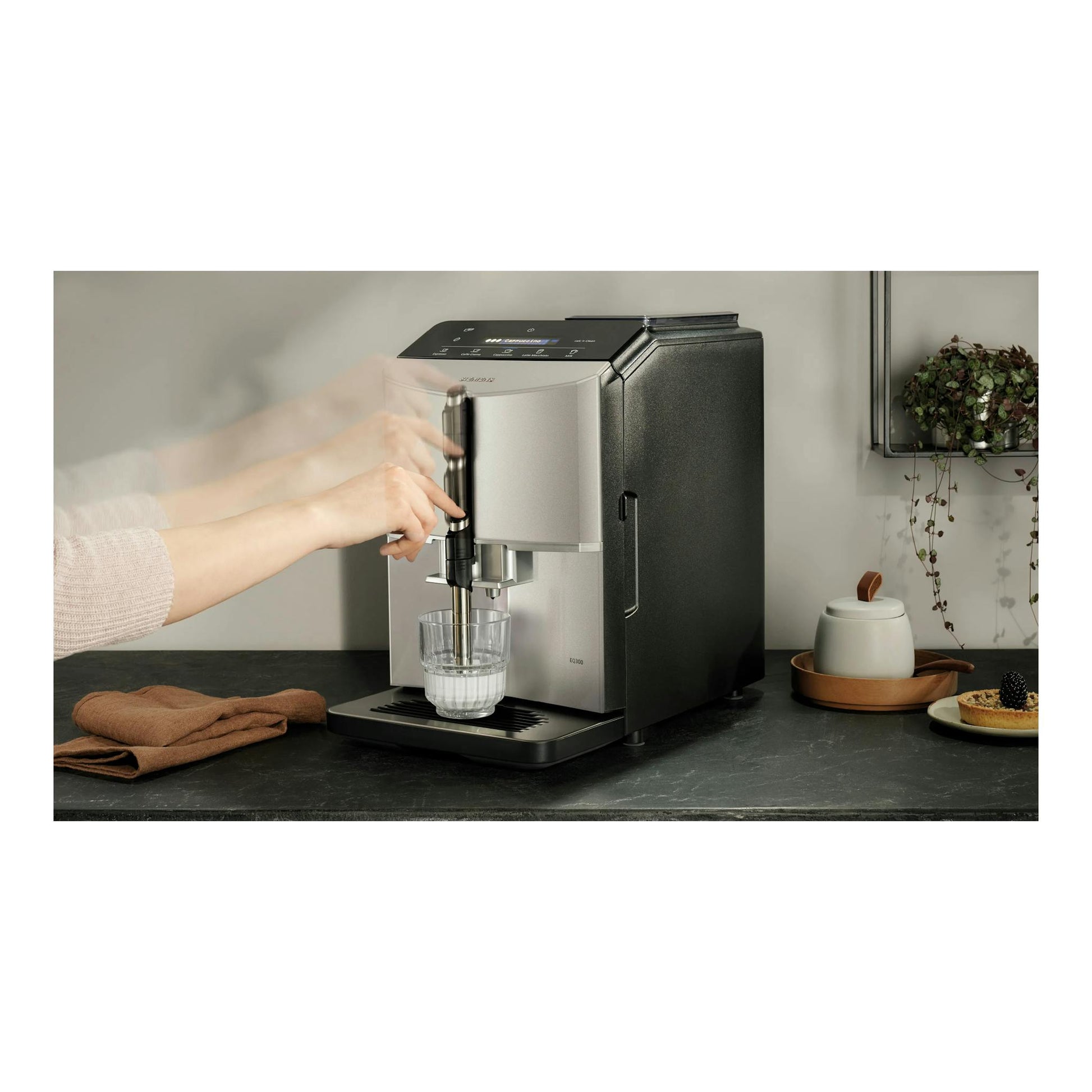 Cafetera superautomática Siemens EQ300 negra y plateada, vista frontal, con una mano colocando un vaso.