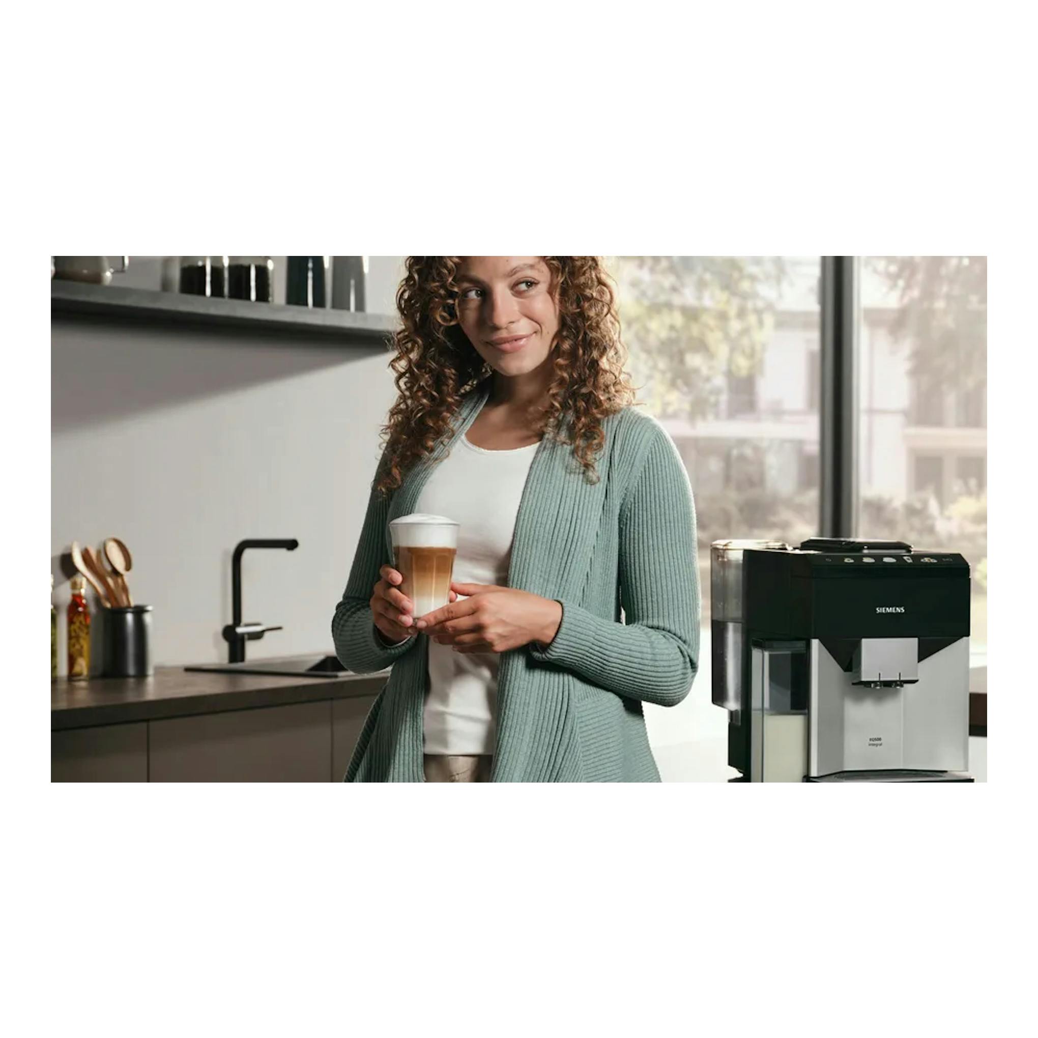 Cafetera superautomática Siemens TQ513R01 negra y plata, en una cocina; una mujer sostiene un café.