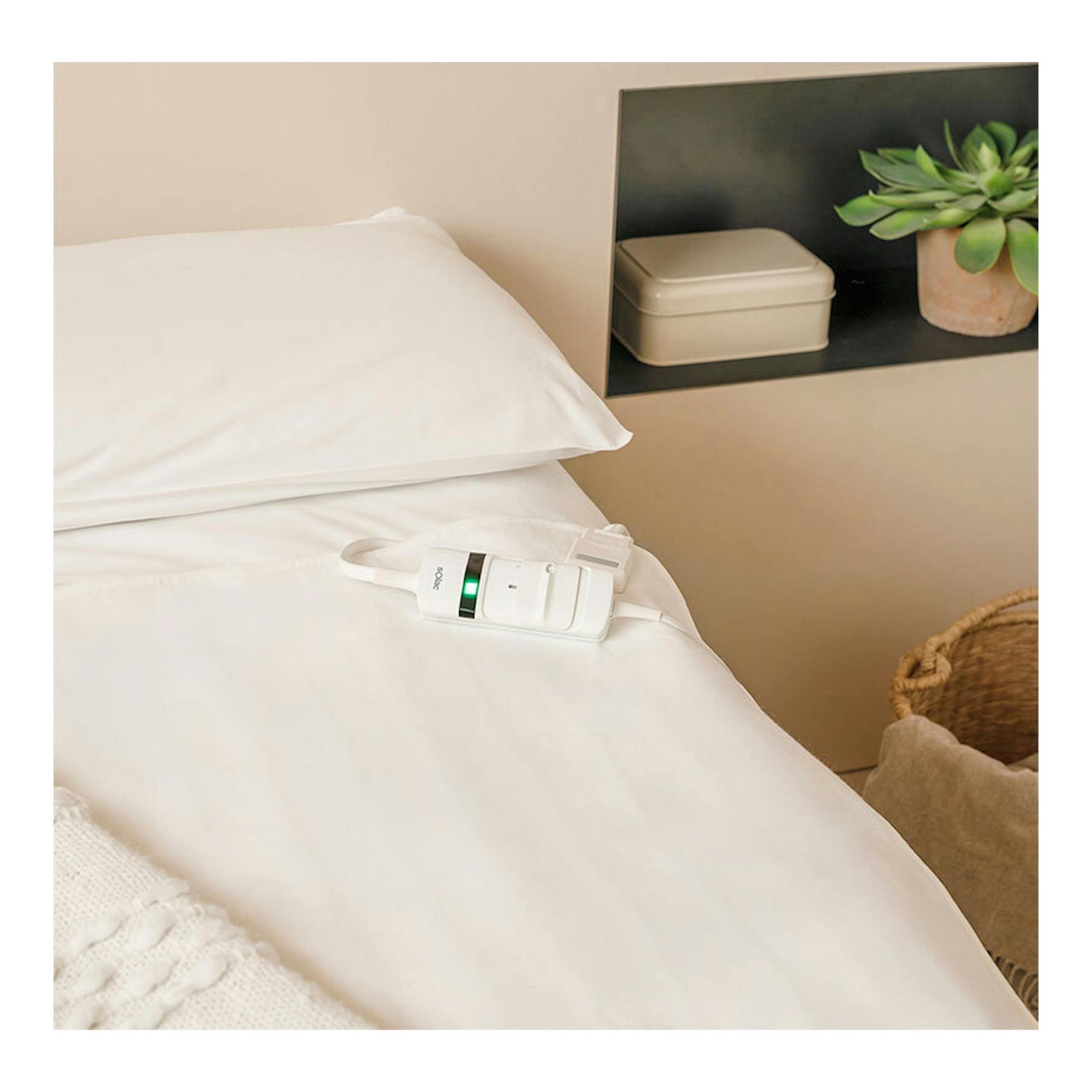 Calientacamas Solac Denmark CT8705 blanco sobre una cama blanca, con mando y luz verde.