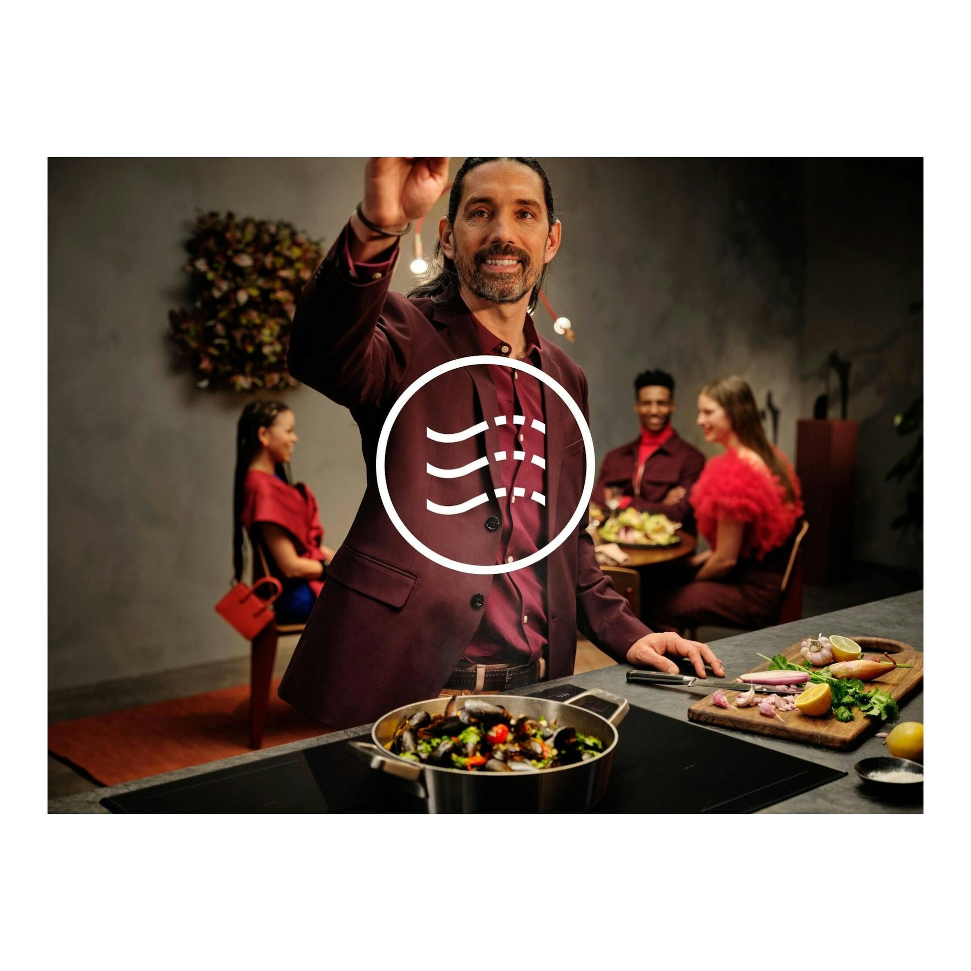 Imagen promocional de campana AEG GV77D81SZ en cocina, con persona cocinando y comensales al fondo.