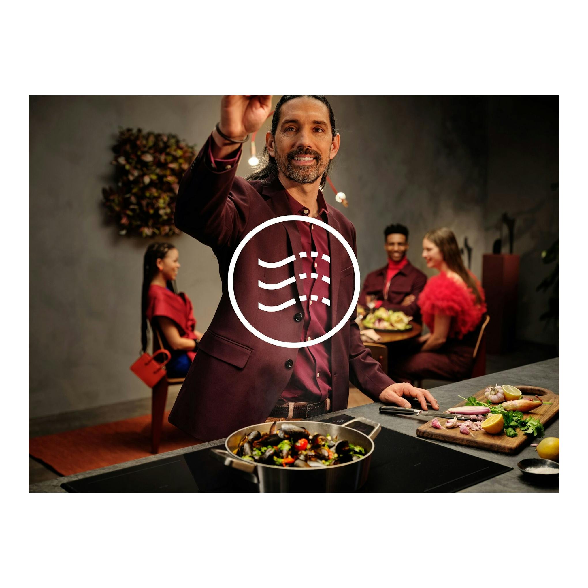 Imagen promocional de campana AEG GV77D81SZ en cocina, con persona cocinando y comensales al fondo.