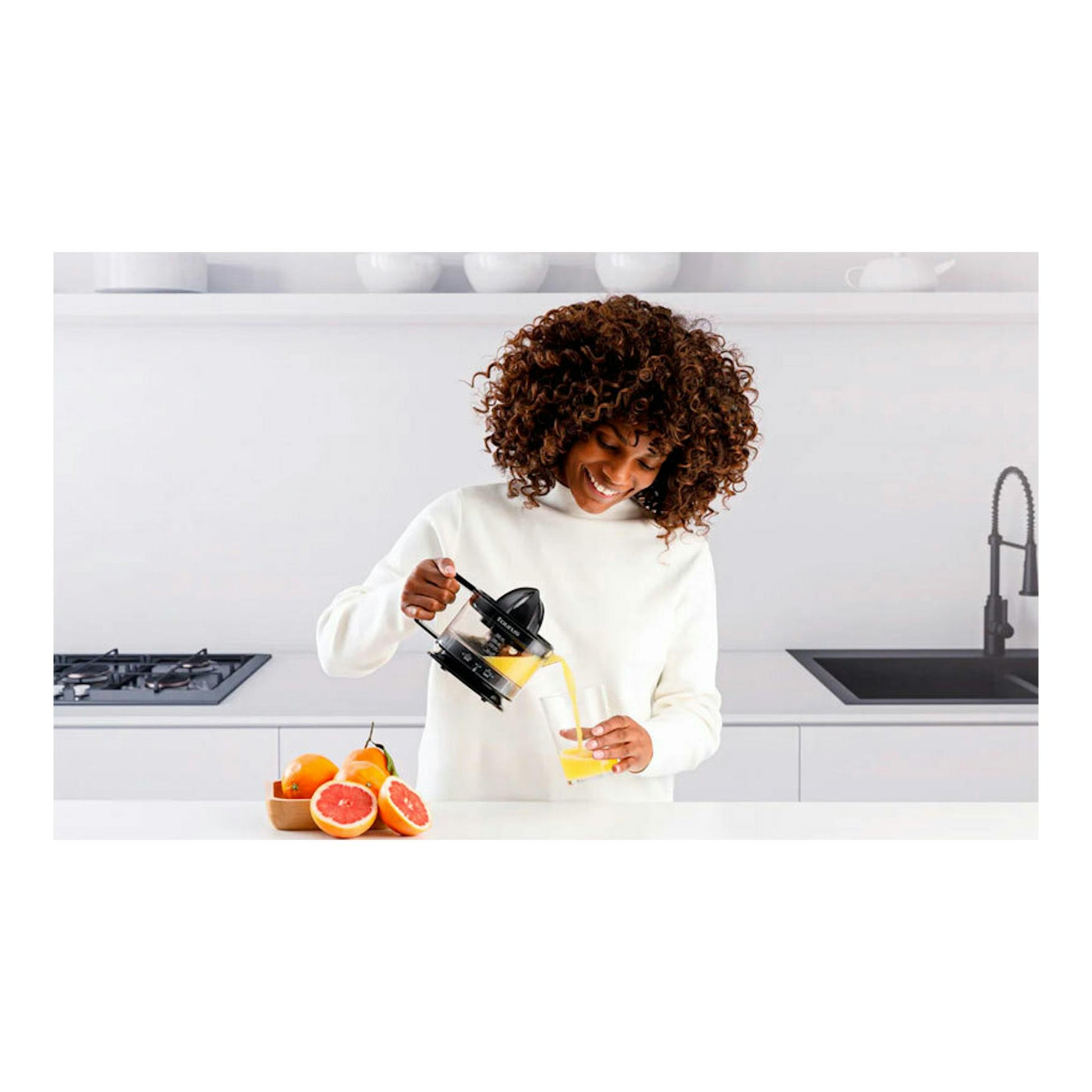 Mujer sirviendo zumo con exprimidor negro Taurus TC-350 Nero en una cocina, con naranjas y pomelos.