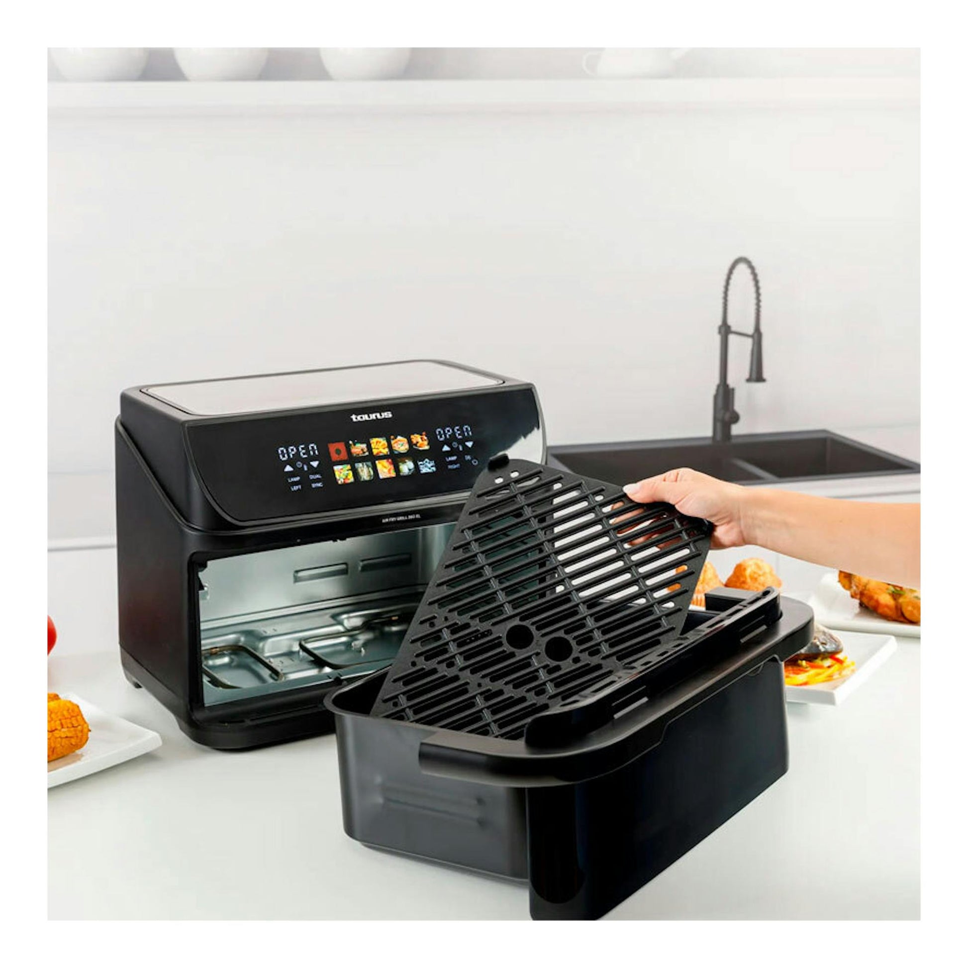 Freidora de aire Taurus Grill 360 negra, vista frontal-3/4, con cubeta extraíble y rejilla en la mano.