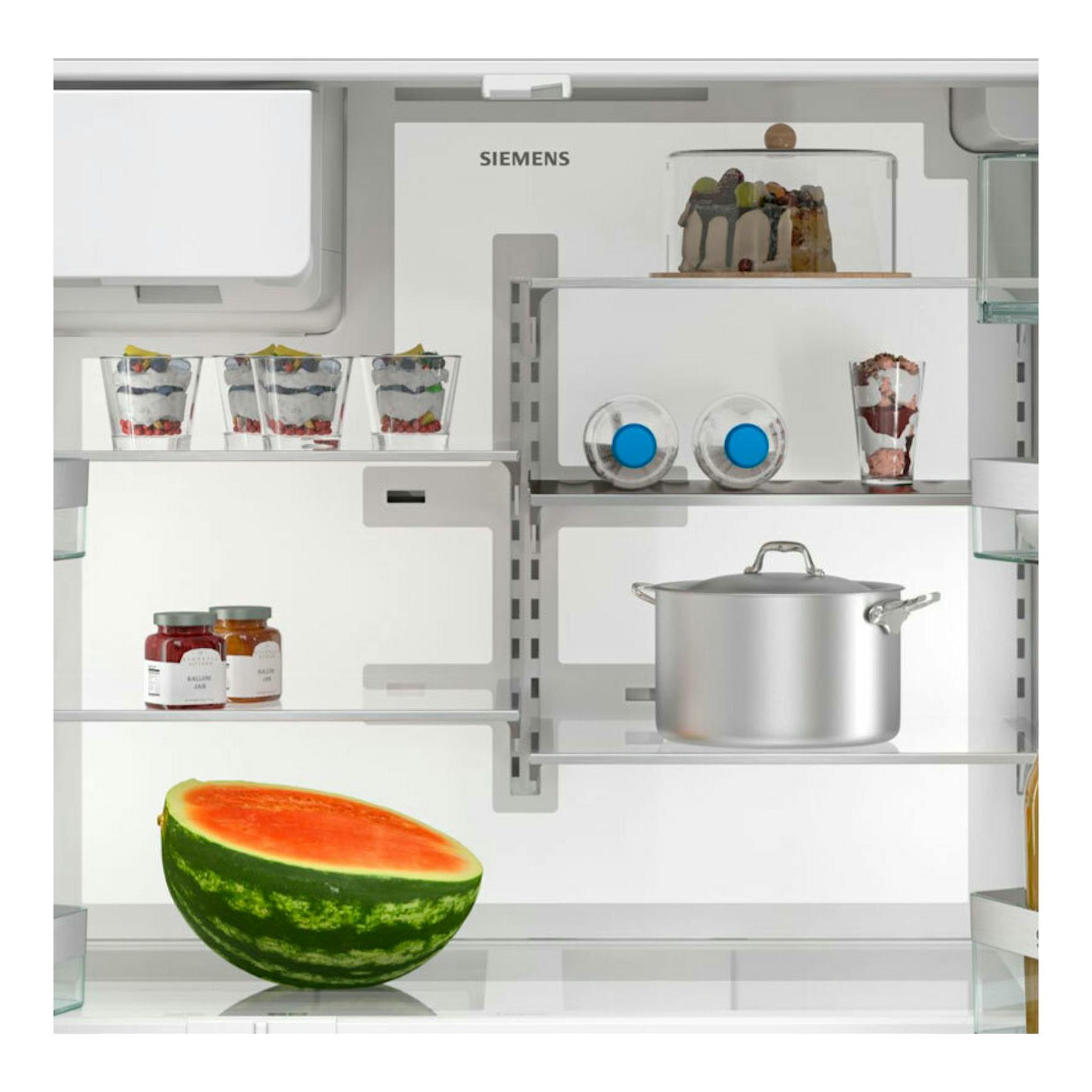 Interior de frigorífico Siemens KF96DPXEA, vista frontal, con estantes blancos, postres, ollas y media sandía.