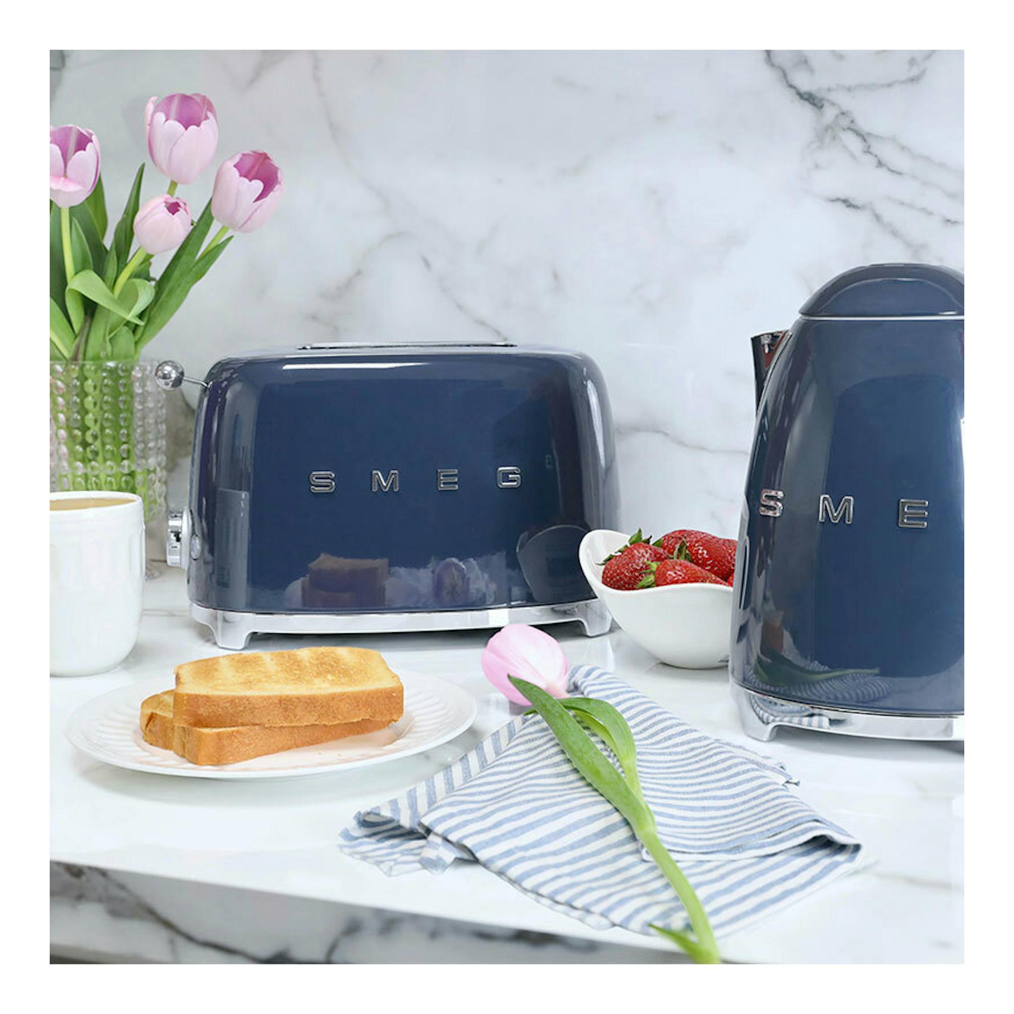 Hervidor Smeg KLF03NBEU azul marino, vista frontal parcial sobre encimera de mármol, junto a tostadora a juego.