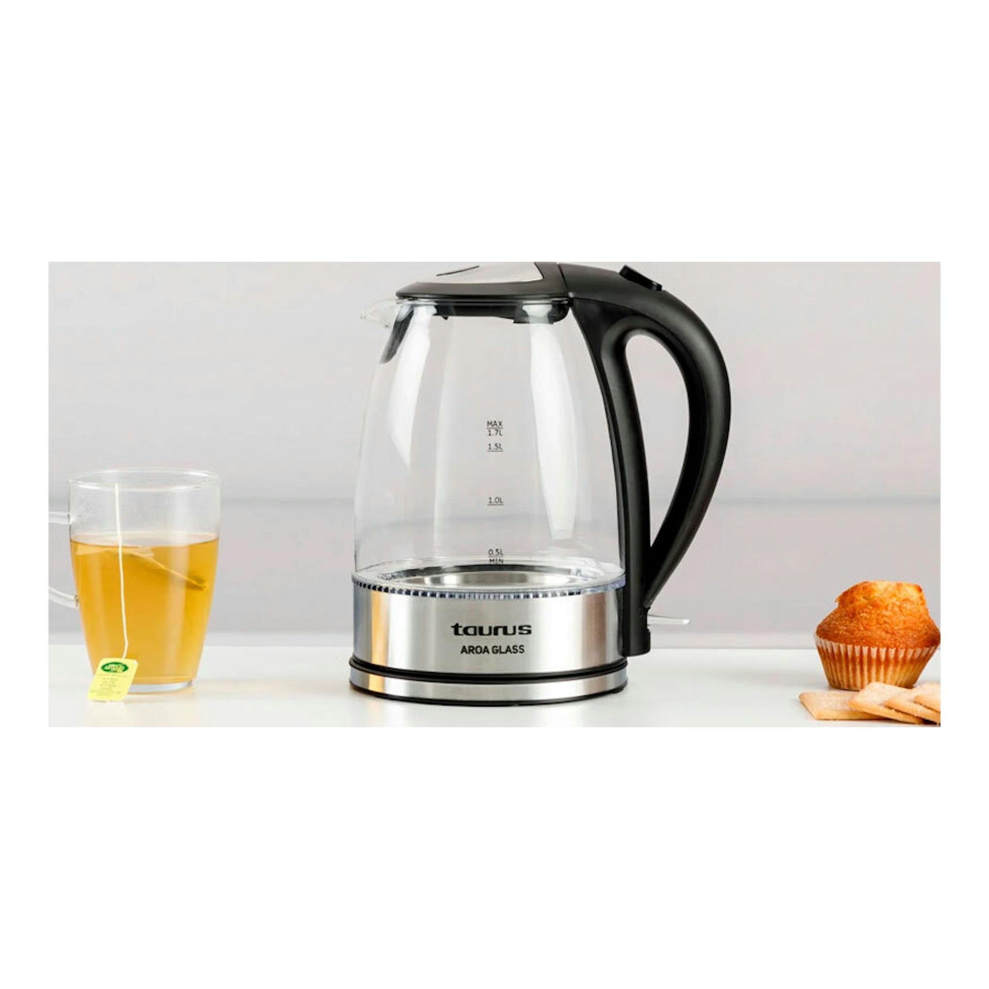 Hervidor Taurus Aroa Glass de vidrio y negro, vista frontal, junto a una taza de té y un muffin.