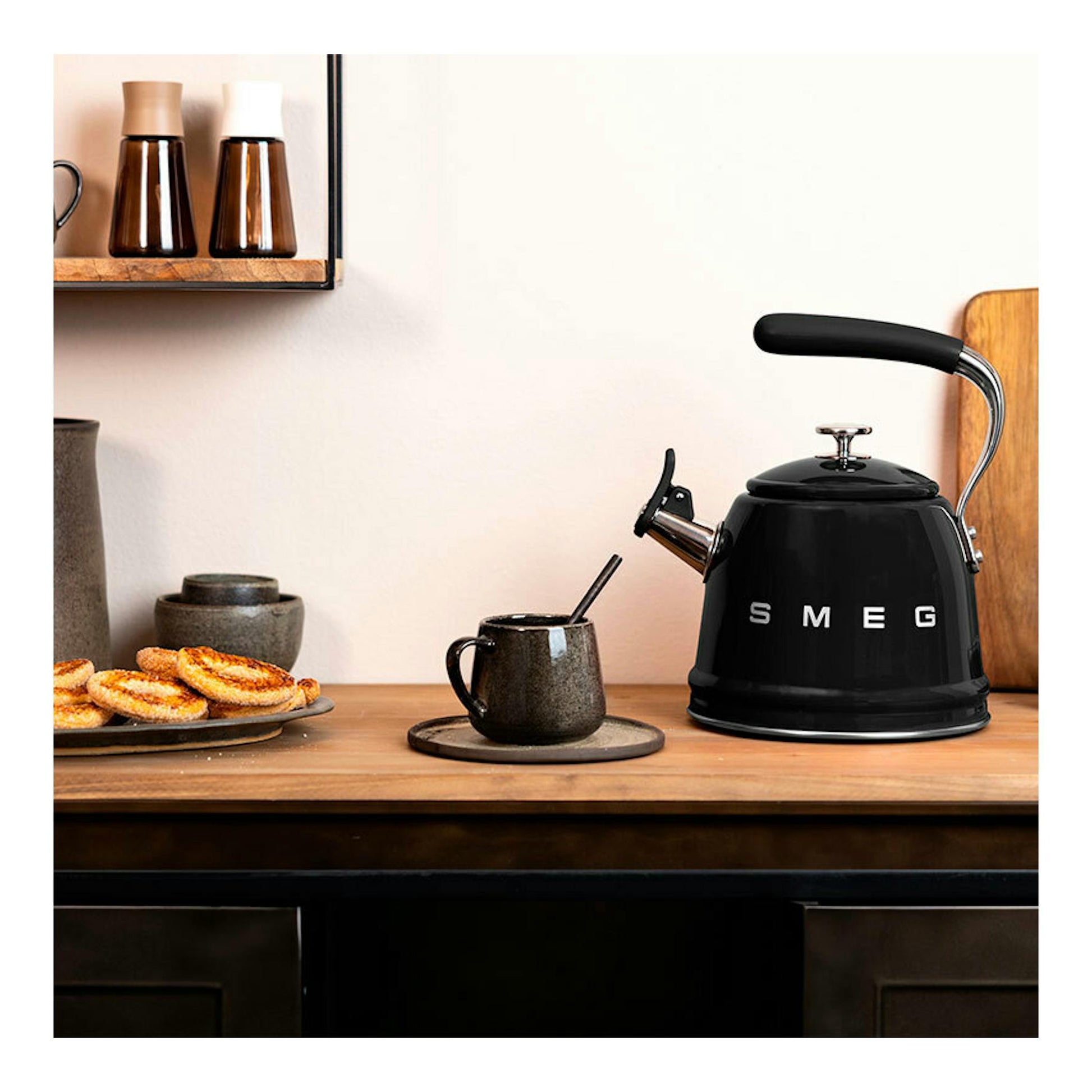 Hervidor silbante Smeg WKF01BL negro, vista frontal tres cuartos sobre encimera de madera.