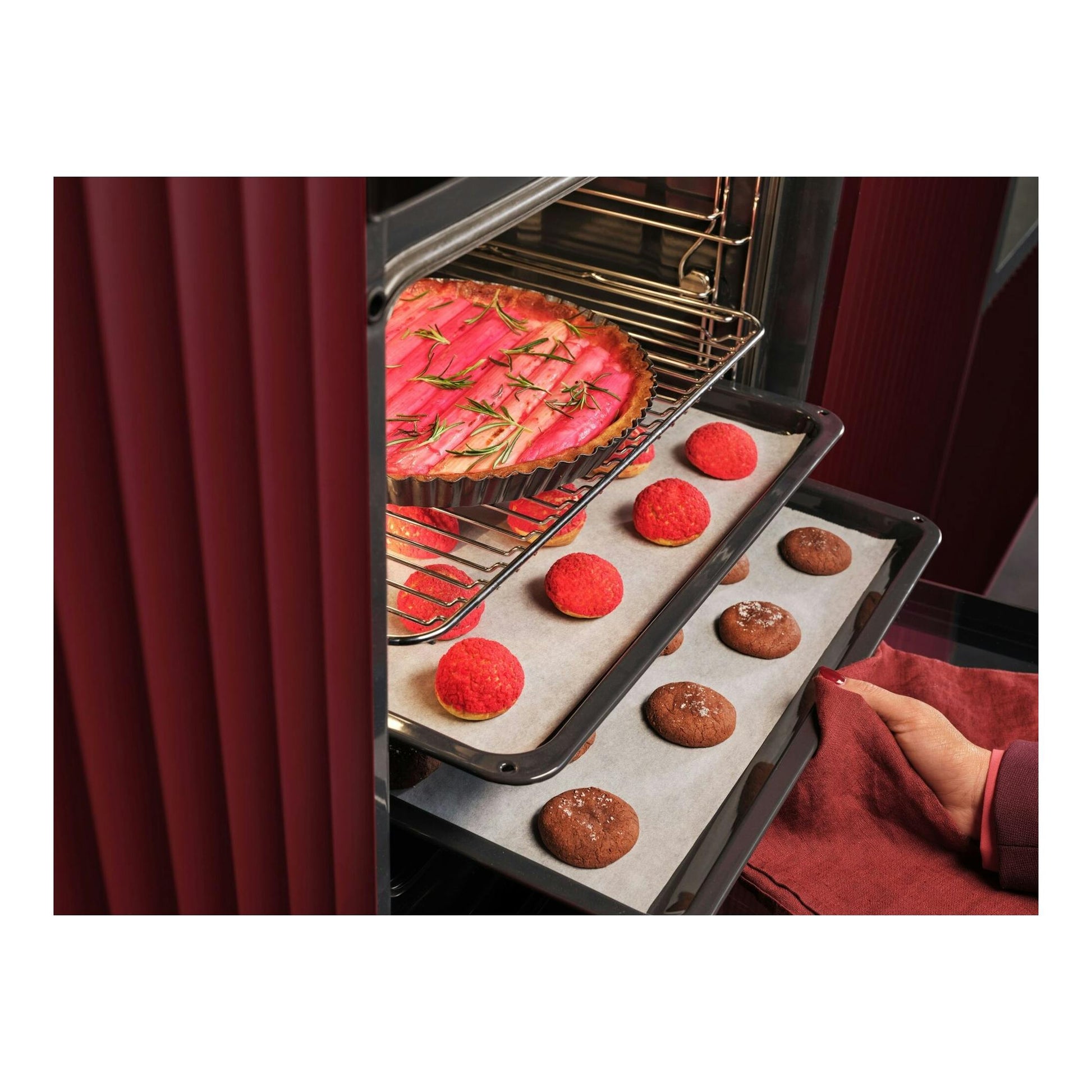 Horno AEG OU5PB43PM abierto, vista frontal del interior con bandejas de galletas y una tarta, en negro y burdeos.