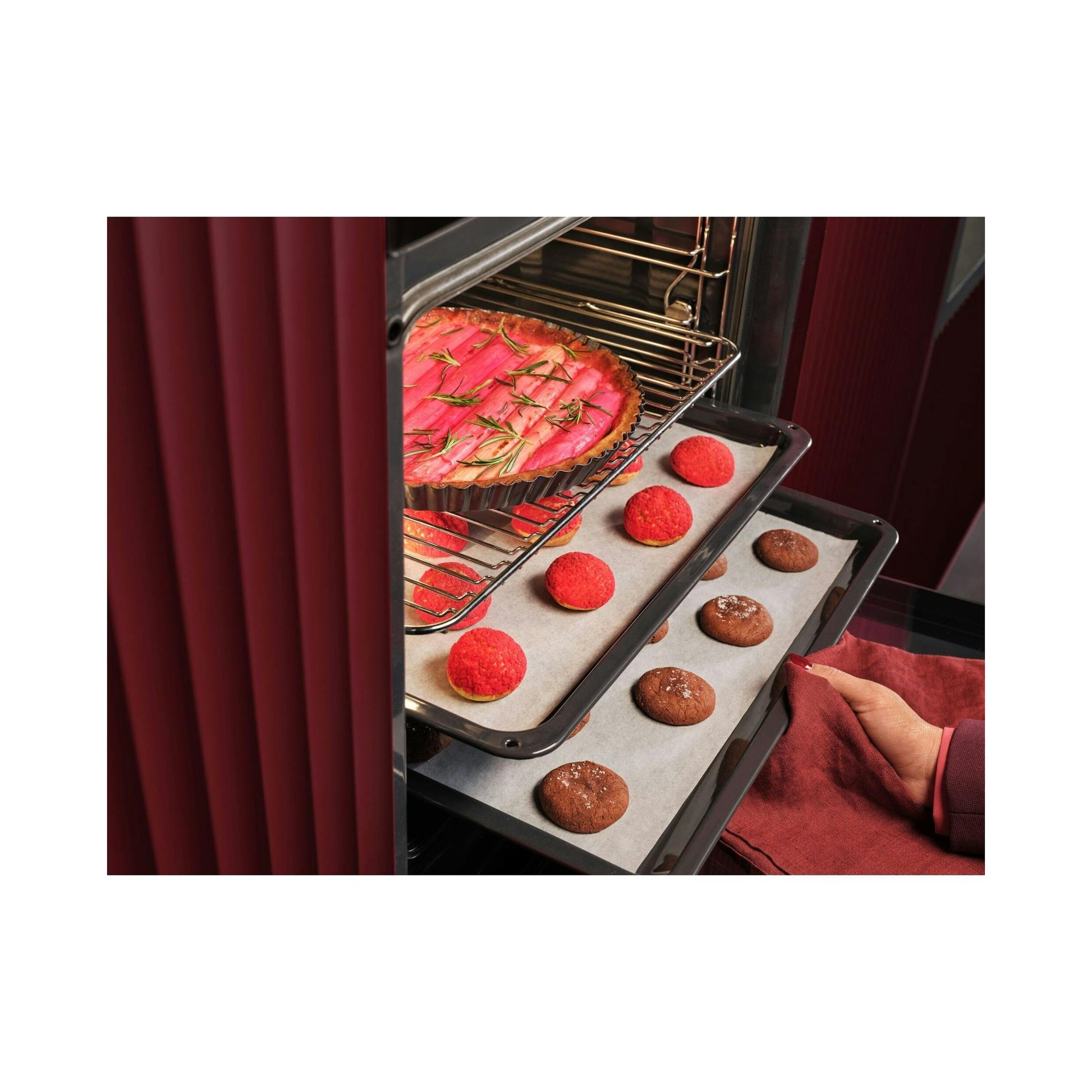 Horno AEG TU5PB41ZPB negro, vista interior con bandejas de repostería y mano con paño rojo.