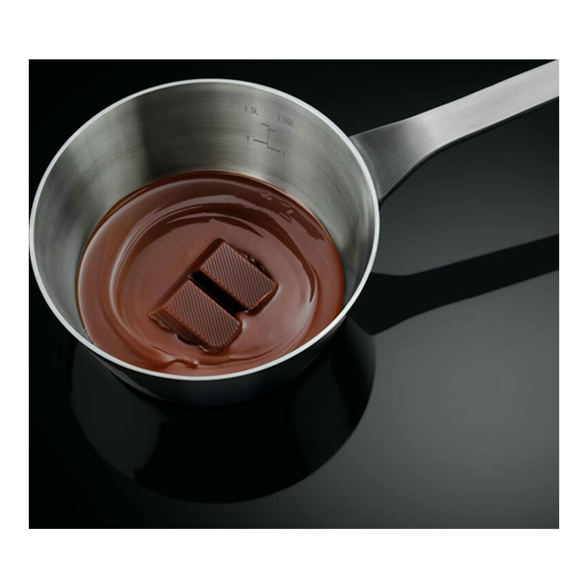 Cazo de acero con chocolate derretido y dos trozos de chocolate, vista cenital sobre fondo negro.