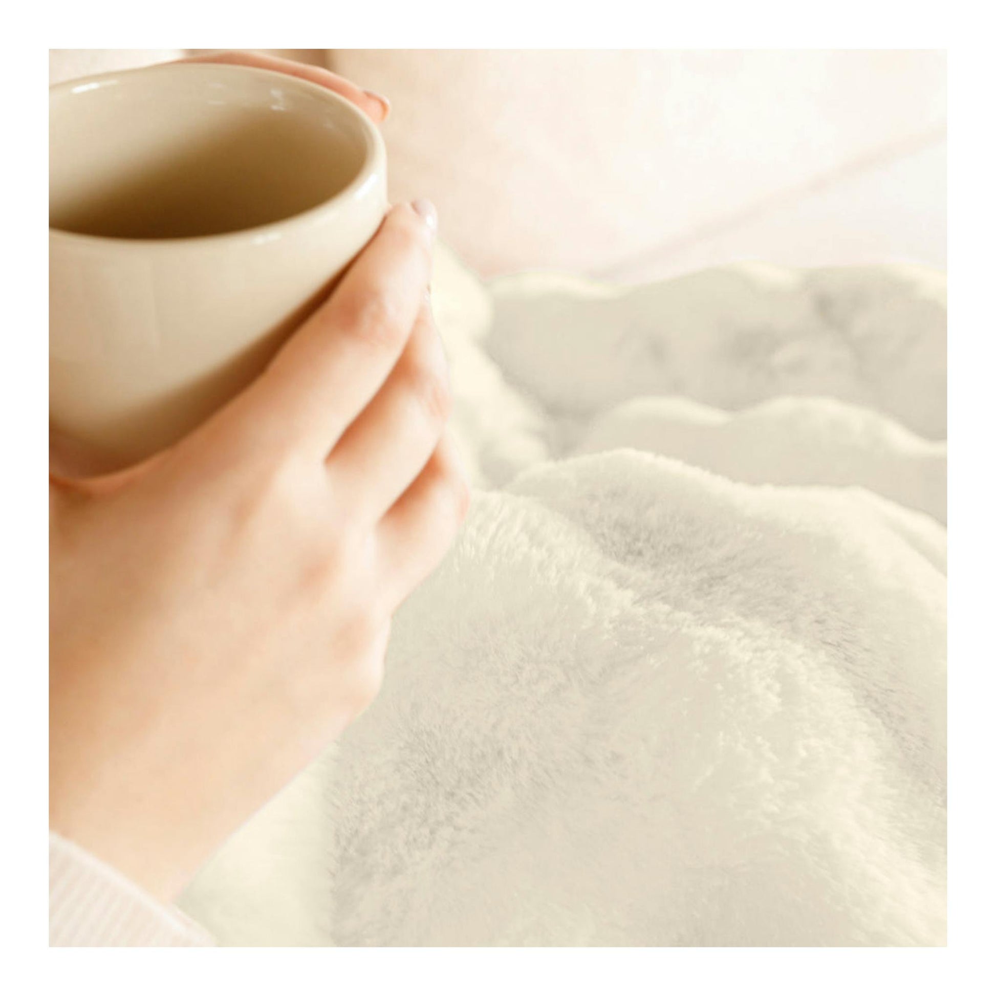 Primer plano de una mano sosteniendo una taza sobre una manta blanca mullida.