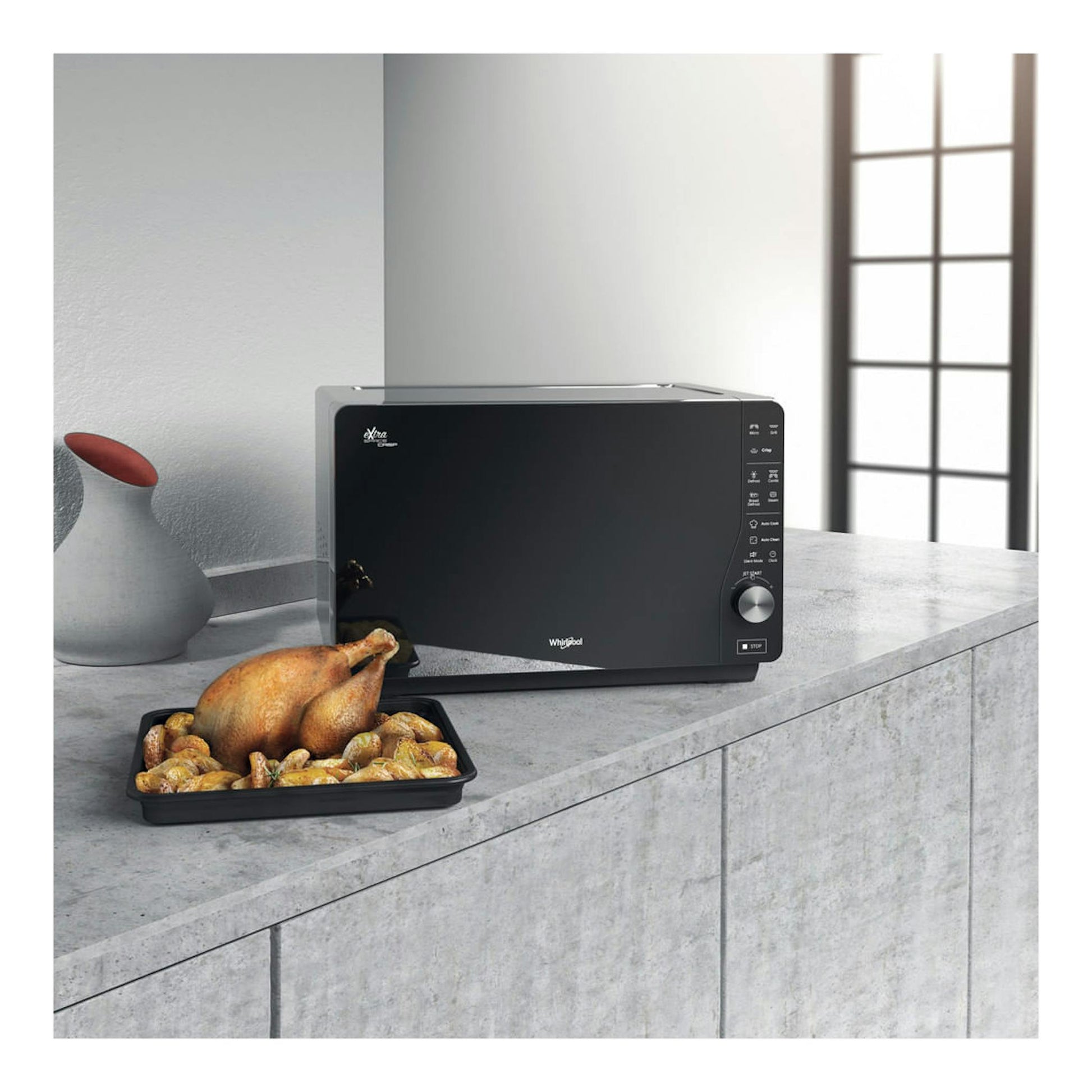 Microondas Whirlpool MWF 427 SL negro, vista frontal, sobre encimera junto a una bandeja con pollo asado.