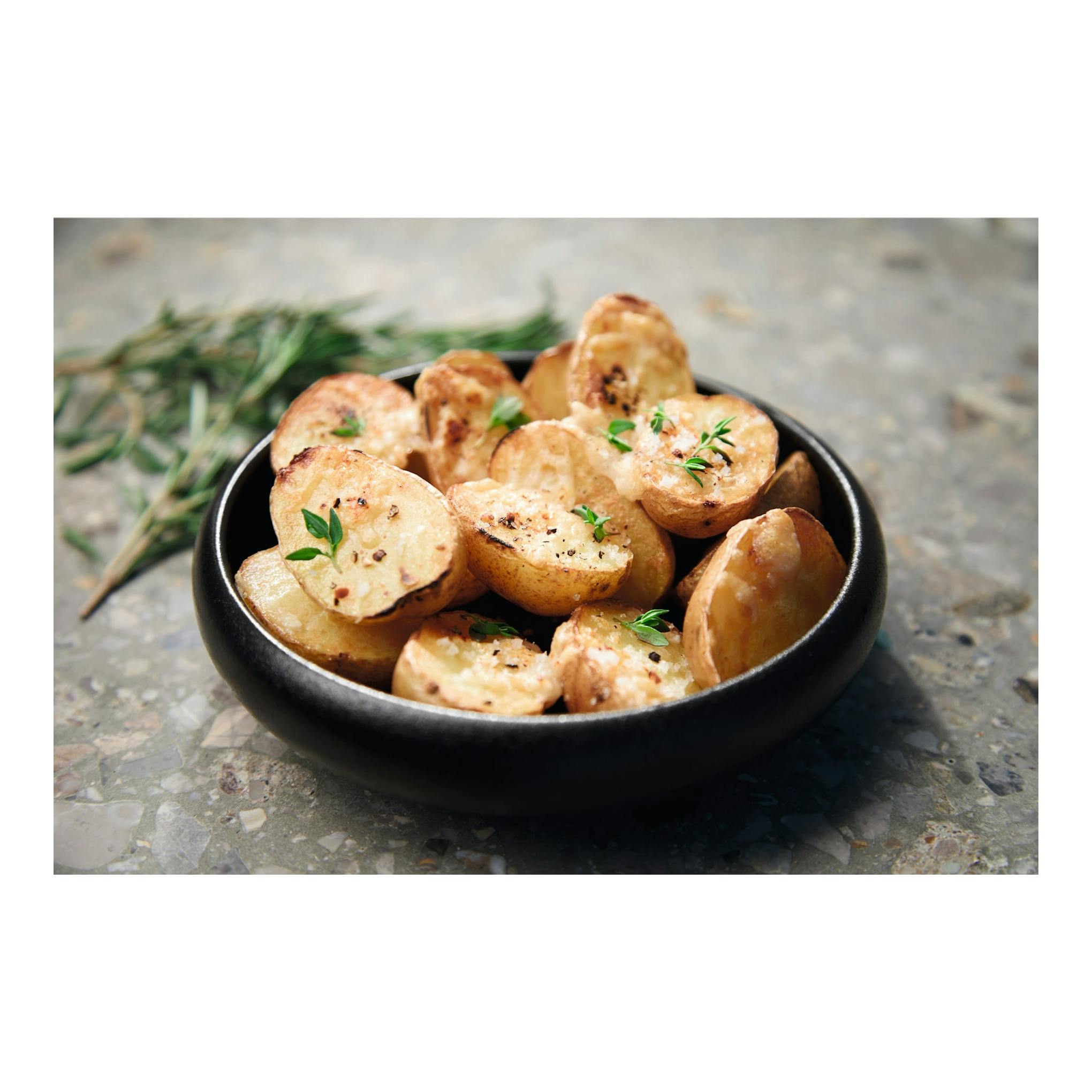 Bowl negro con patatas asadas y hierbas sobre superficie de piedra.