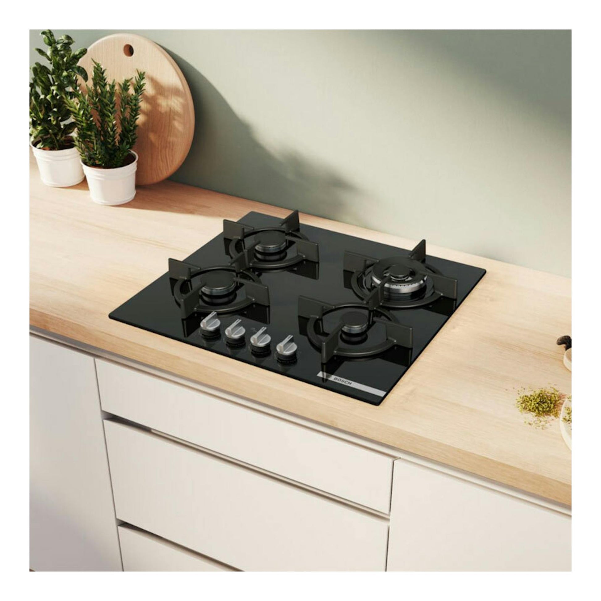 Placa de gas Bosch PPH6A6I10 negra, vista superior oblicua, con 4 fuegos sobre encimera clara.