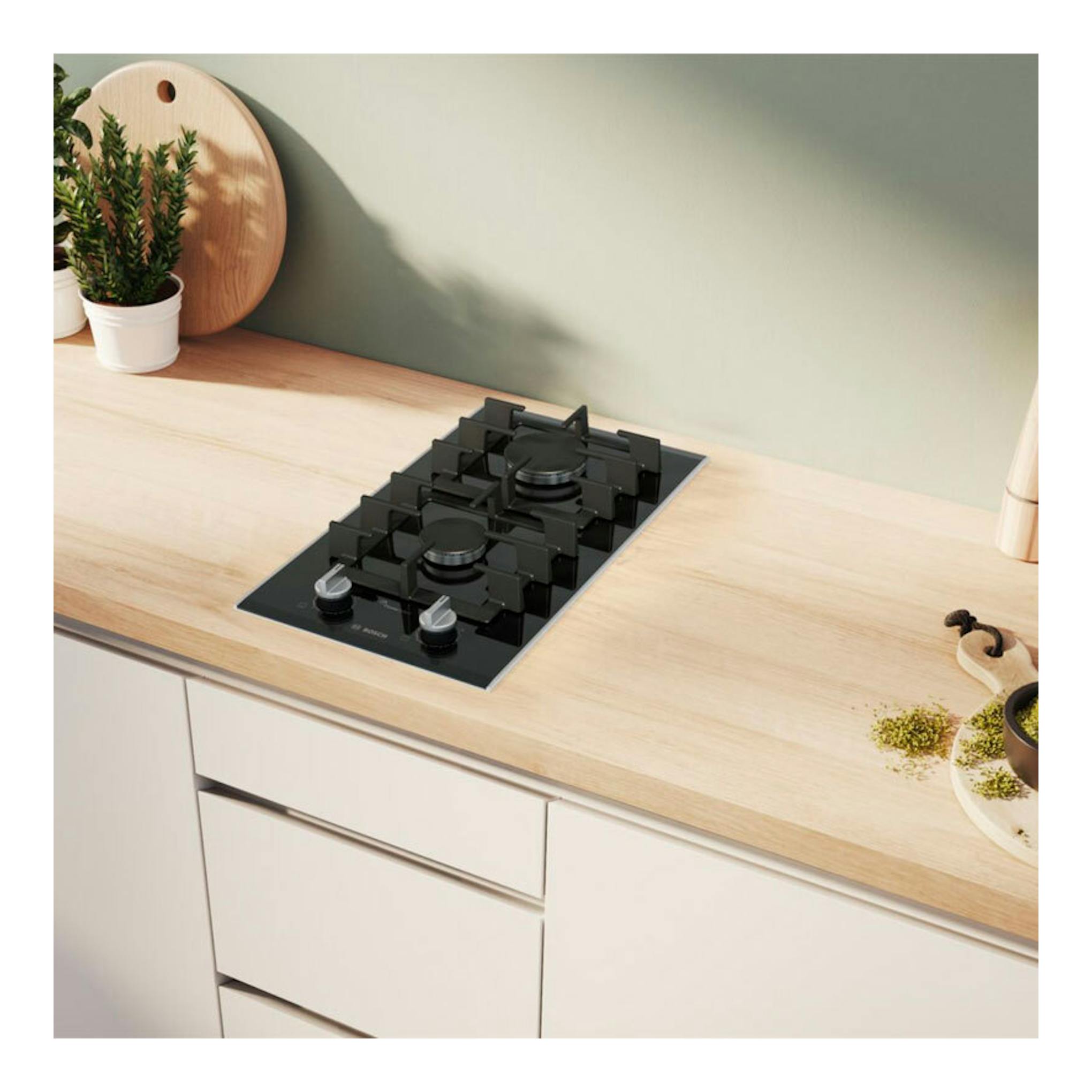 Placa de gas Bosch PRB3A6I40 negra, vista superior inclinada, empotrada en encimera de madera clara.