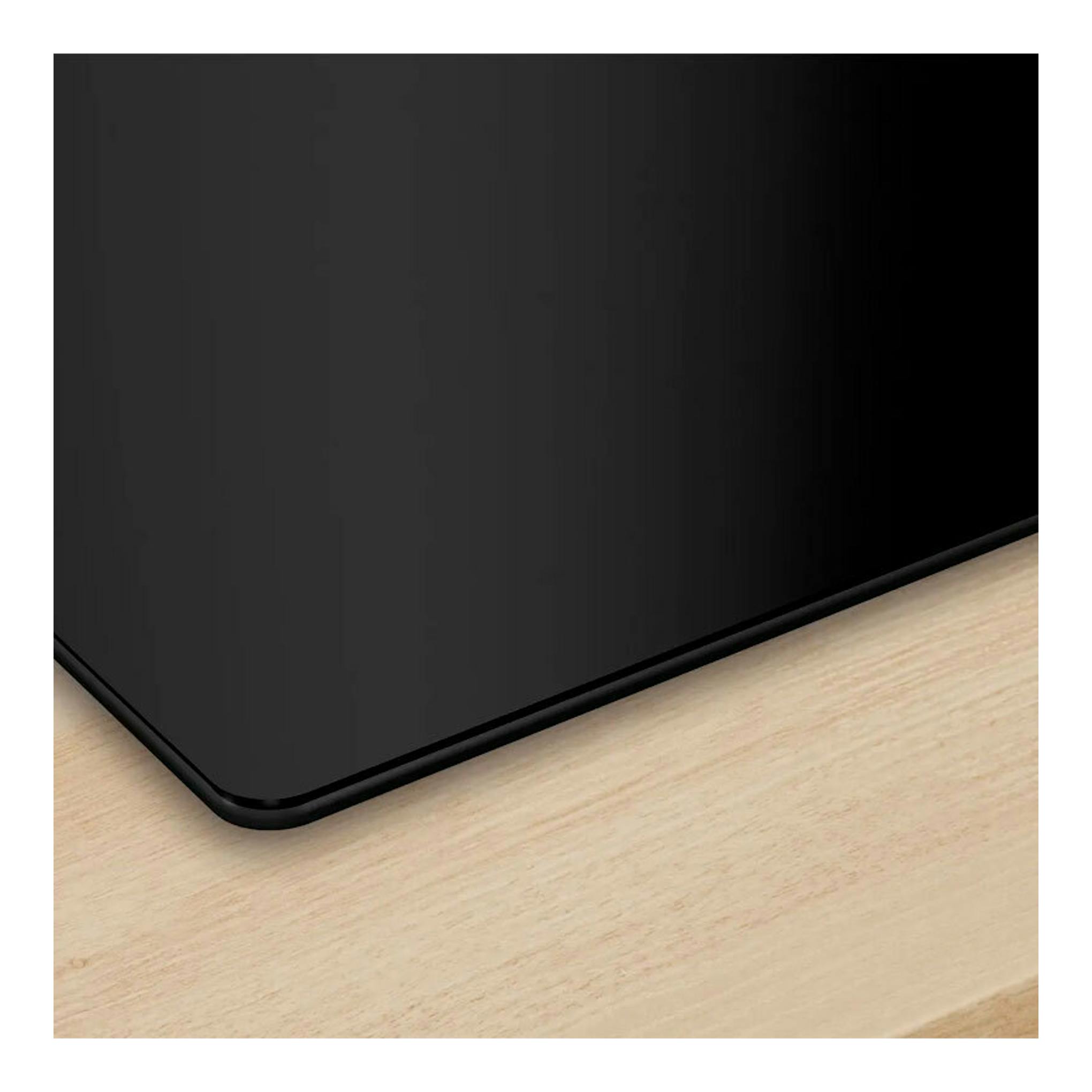 Placa de inducción Bosch PID61RHB1E negra, primer plano de una esquina sobre superficie de madera.