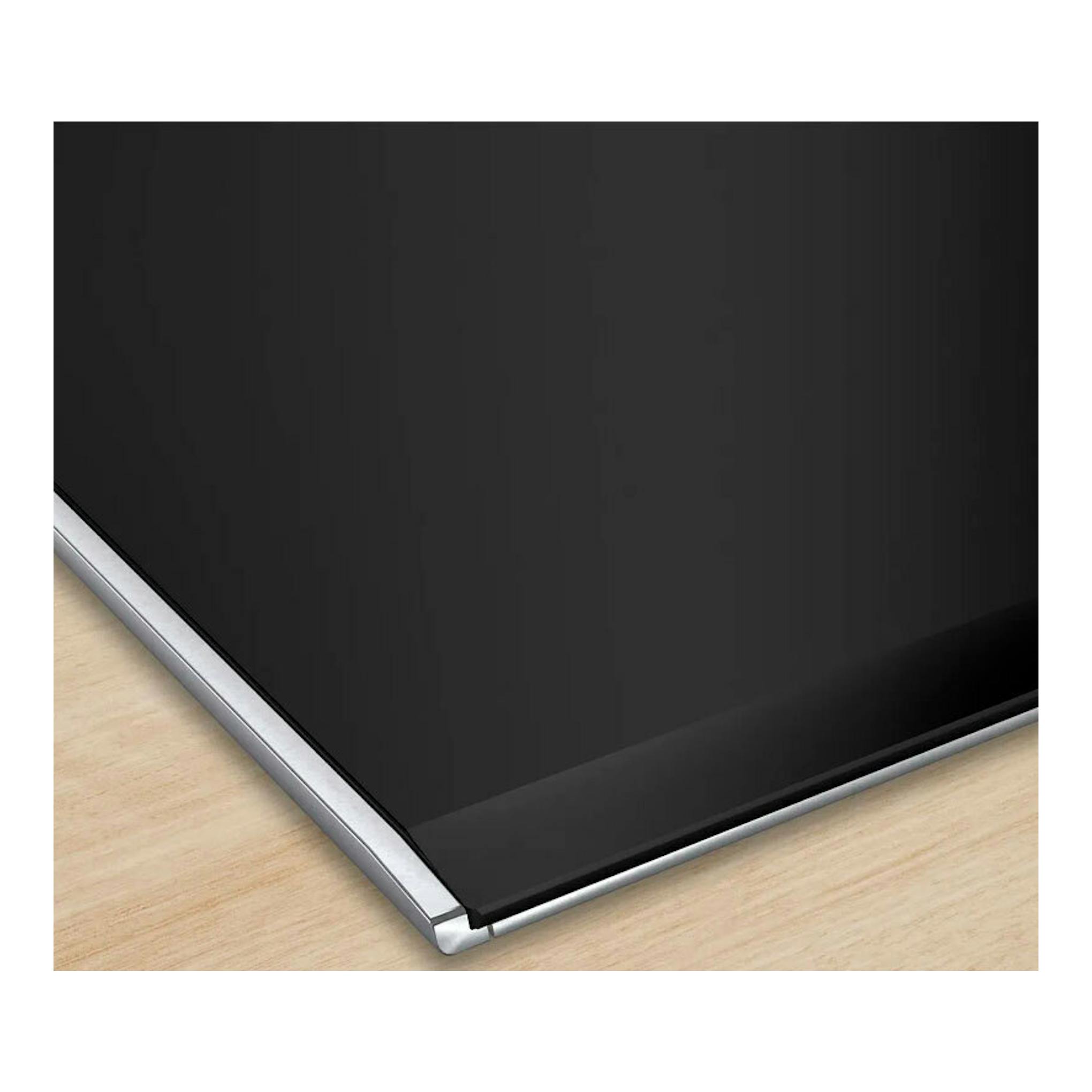 Placa de inducción Bosch PXV875DV1E negra, vista en detalle de la esquina con borde de acero sobre madera.