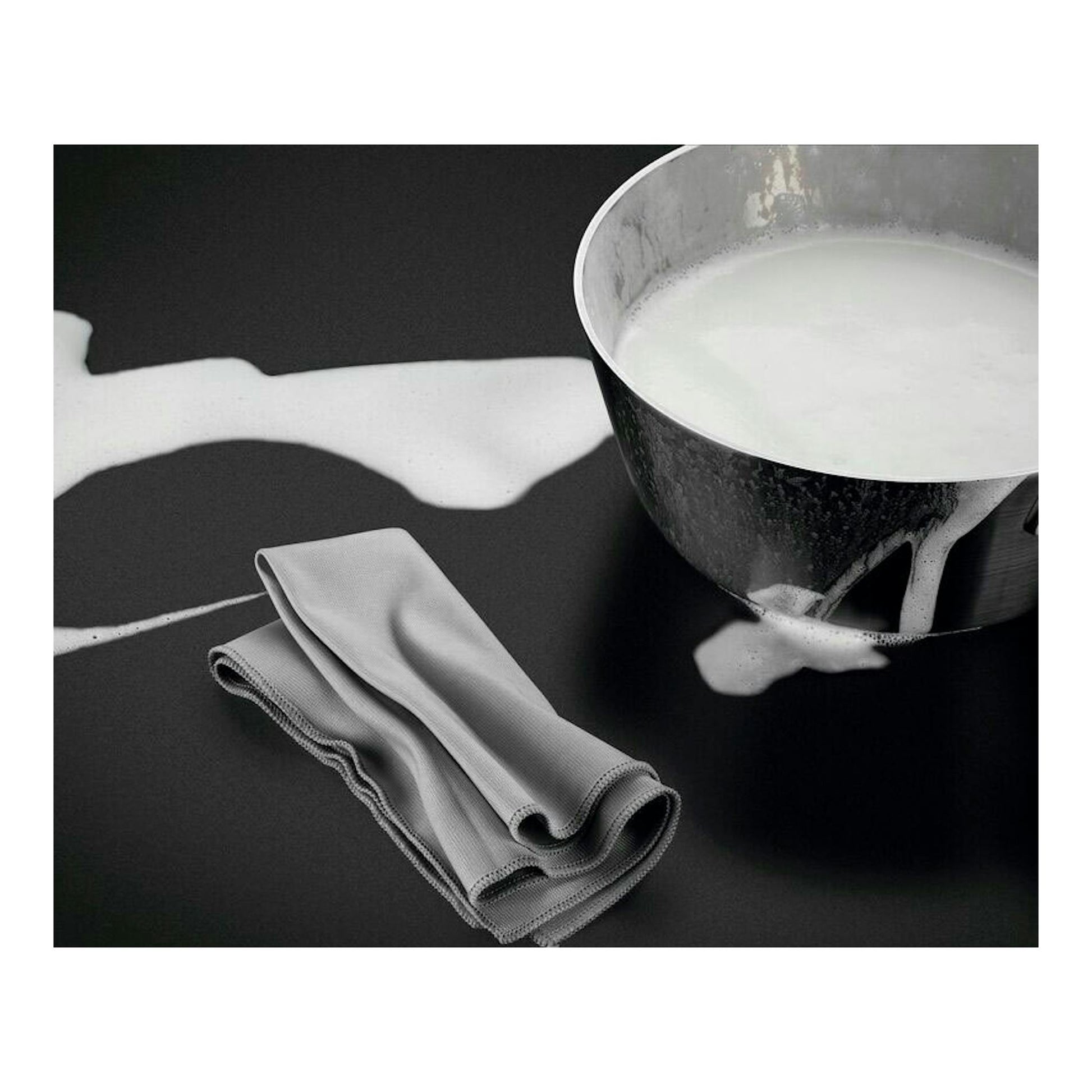 AEG TN63IV00CB, placa de inducción negra con un cazo derramando leche y un paño gris.