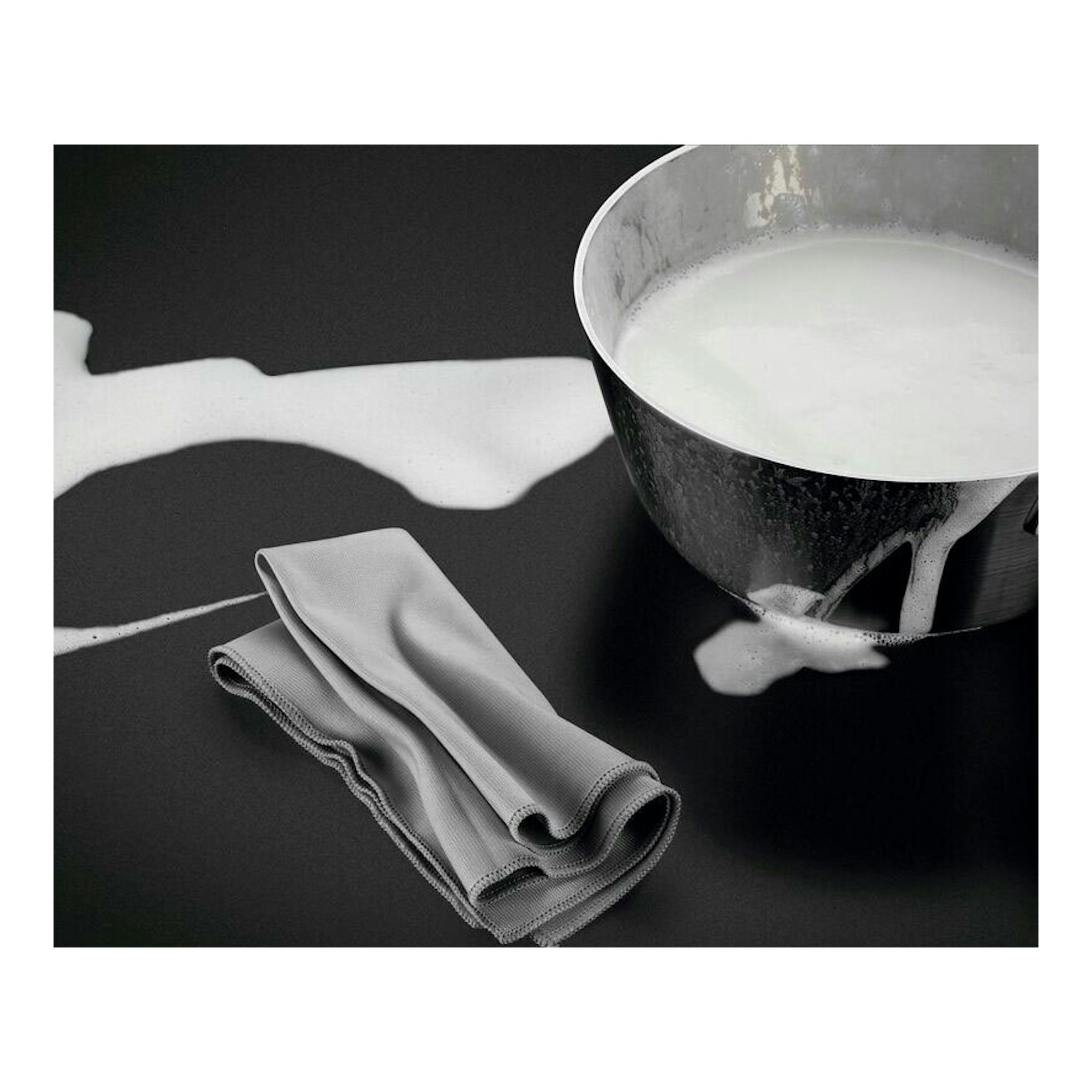 AEG TN63IV00CB, placa de inducción negra con un cazo derramando leche y un paño gris.