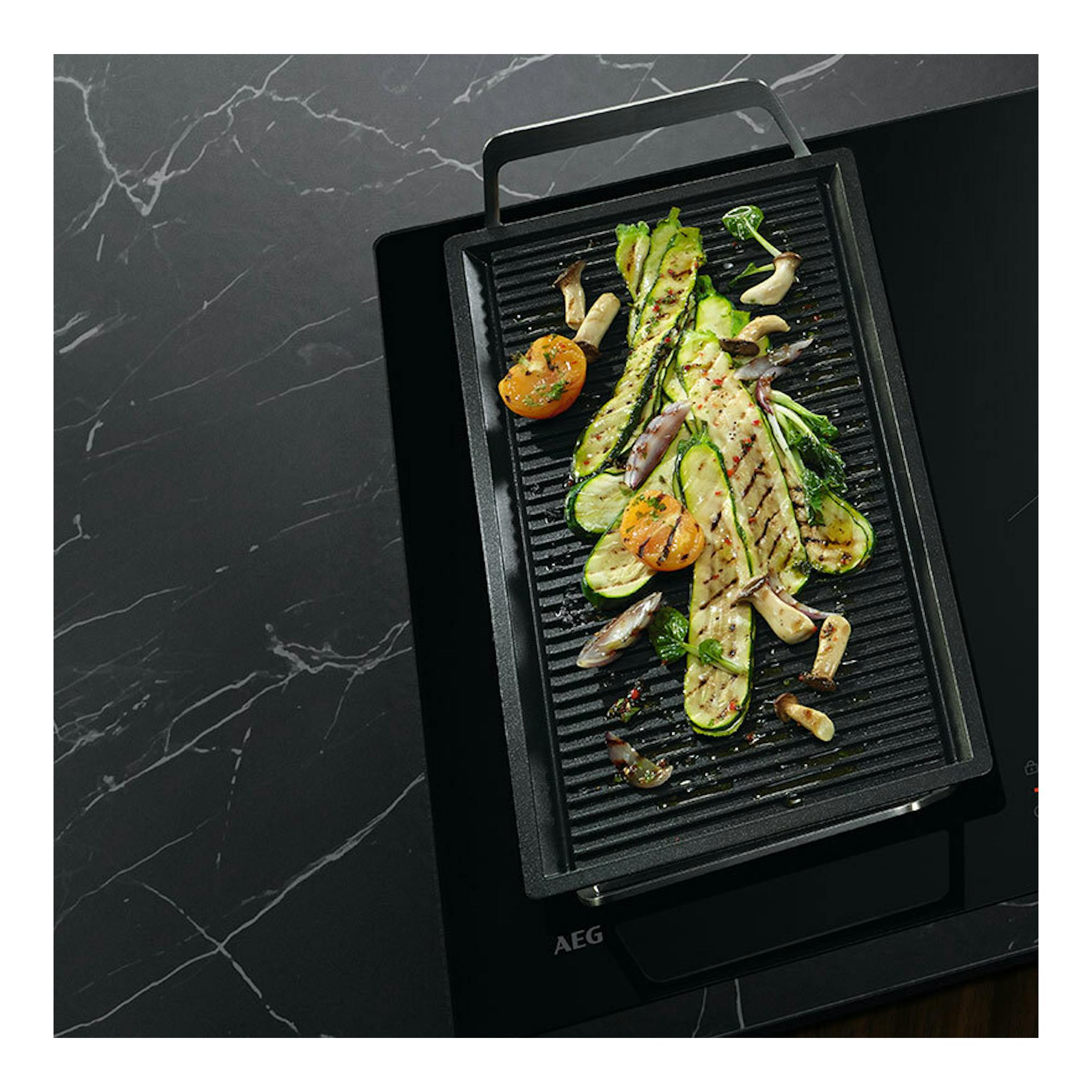 Placa de inducción AEG TO84IU0FFB negra, vista cenital con sartén grill y verduras a la parrilla.