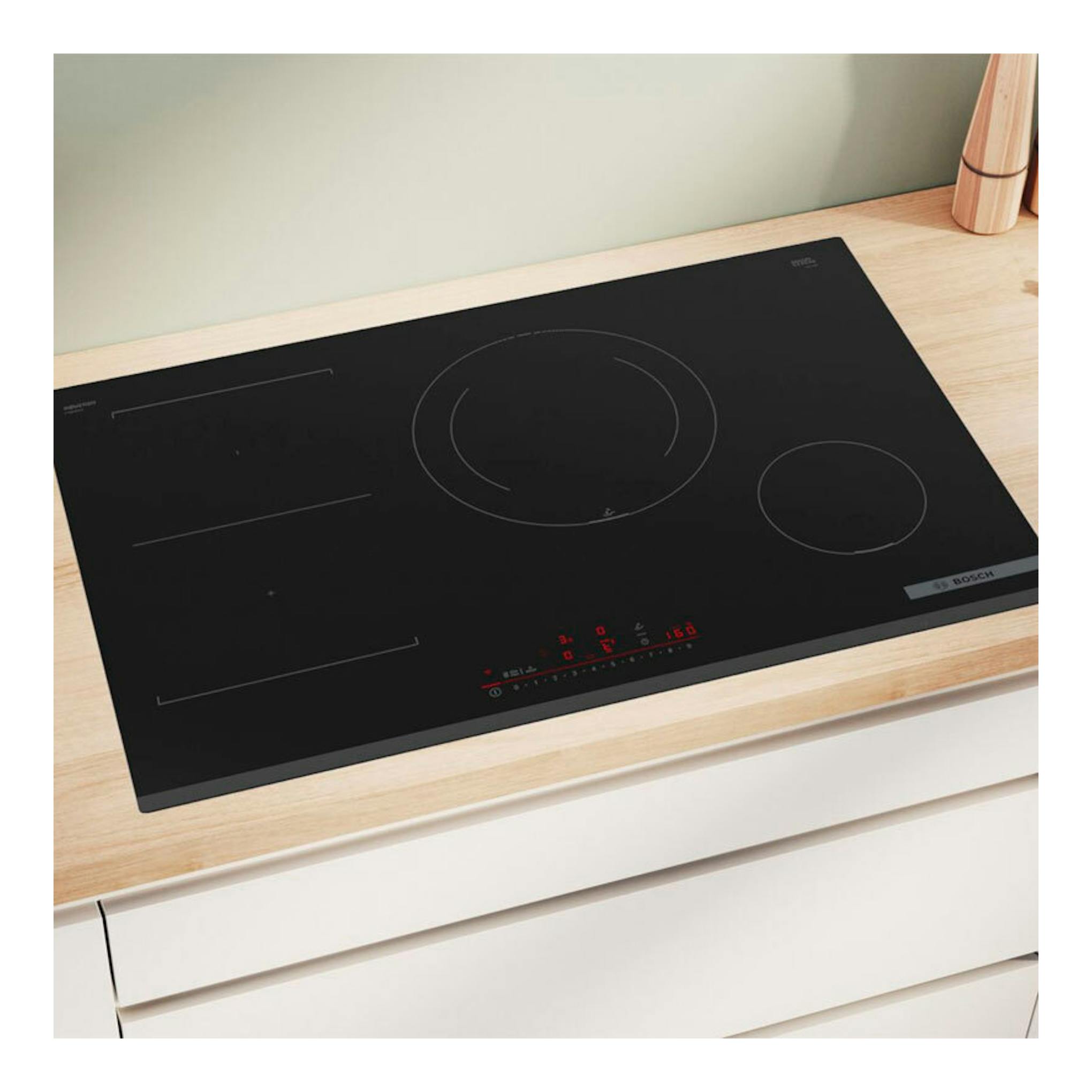 Placa de inducción Bosch PVS831HC1E negra, vista en ángulo sobre encimera de madera, con mandos táctiles rojos.