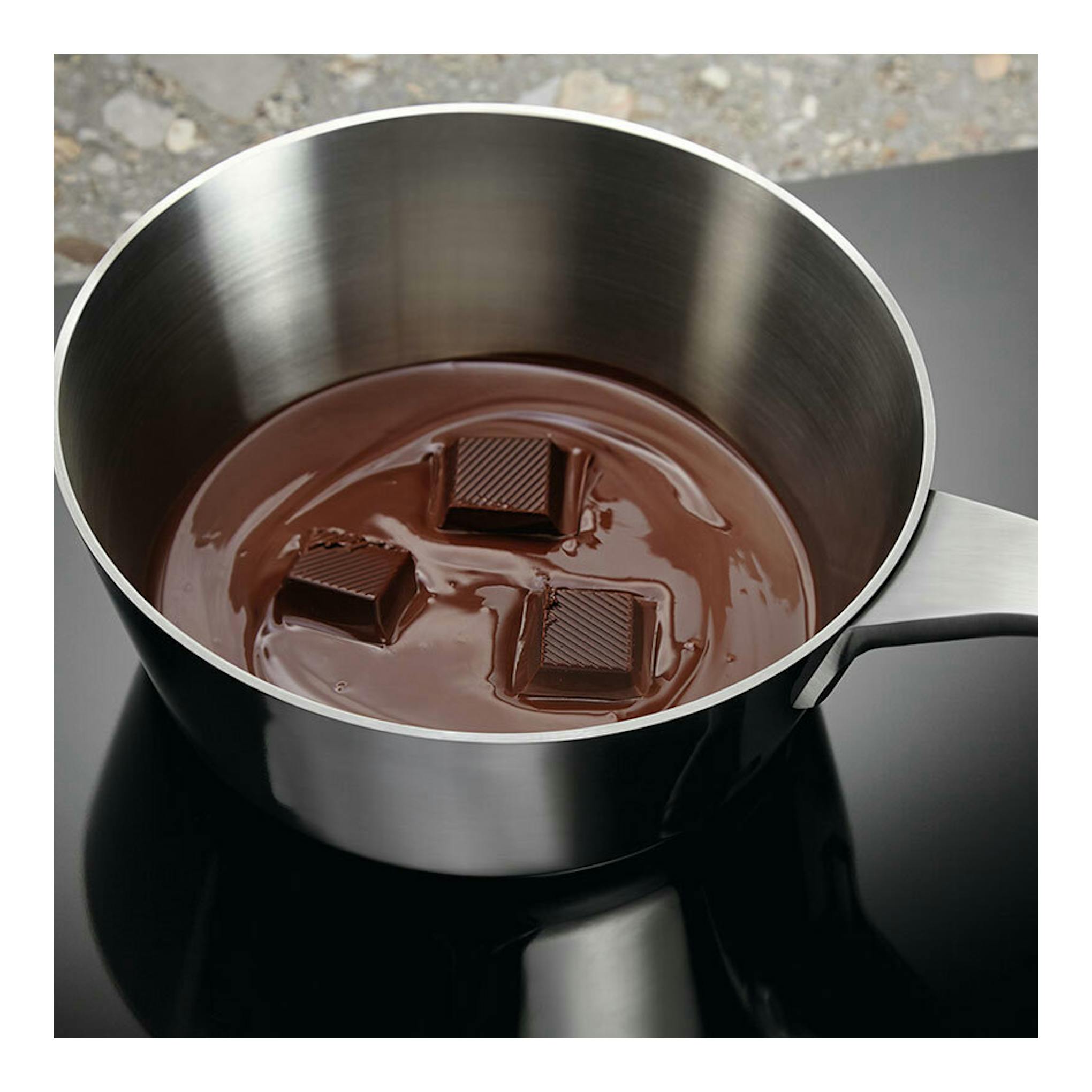 Placa de inducción Electrolux EIV633 negra, vista cenital parcial, con cazo de acero y chocolate fundido.