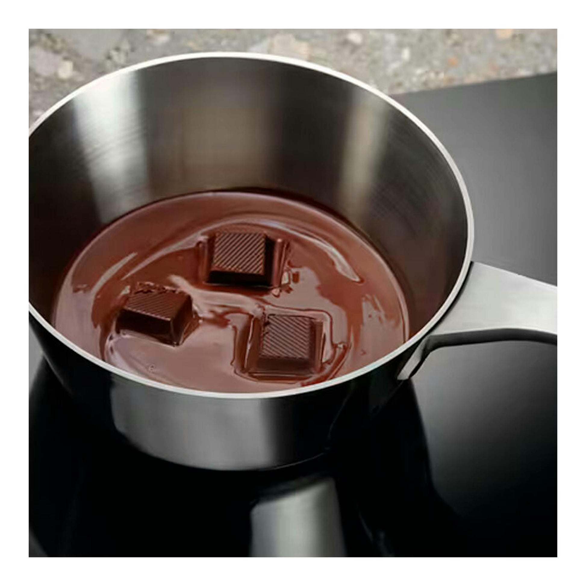 Placa de inducción Electrolux LIT60336CK negra, vista cenital parcial, con cazo de acero y chocolate.
