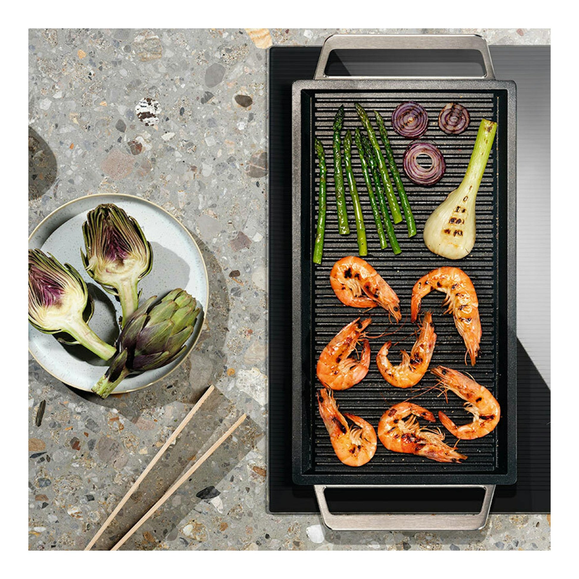 Electrolux LIV63340CK: placa de inducción negra, vista cenital, con plancha grill y gambas, espárragos y alcachofa.