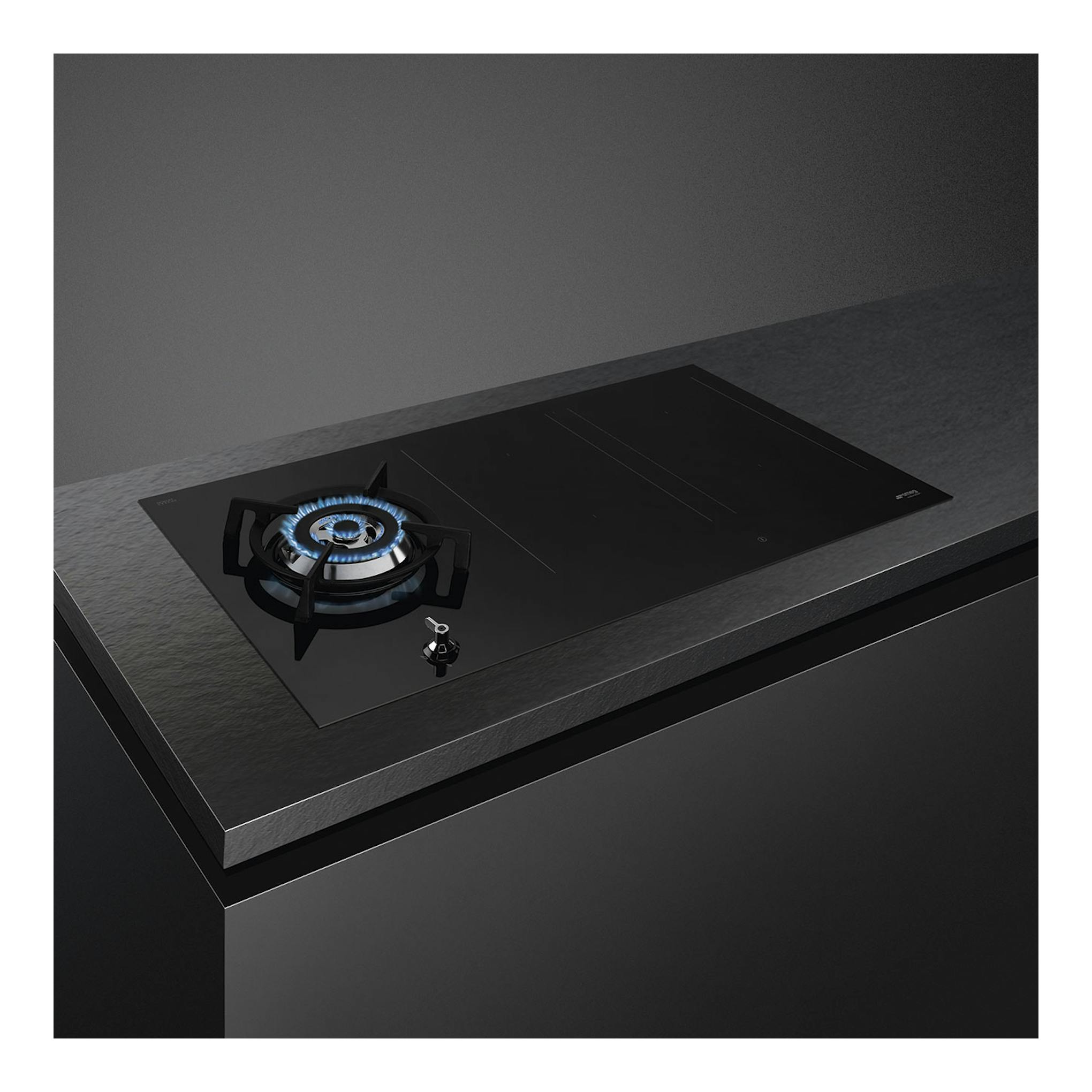 Placa mixta Smeg PM3953D negra, vista en ángulo superior, con quemador de gas encendido y zona de inducción.