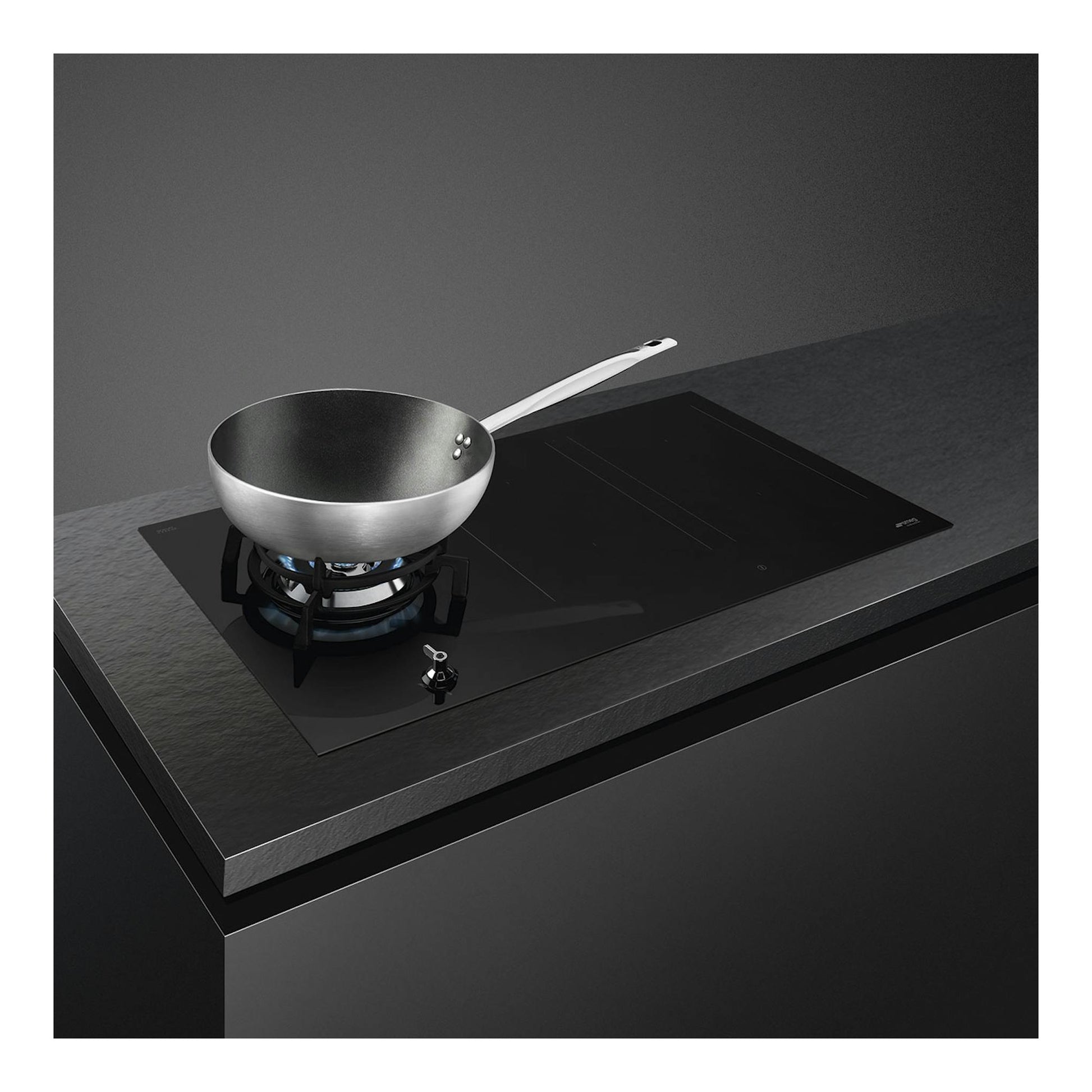 Placa mixta Smeg PM3953D negra, vista en ángulo, con wok sobre quemador de gas y zona de inducción.